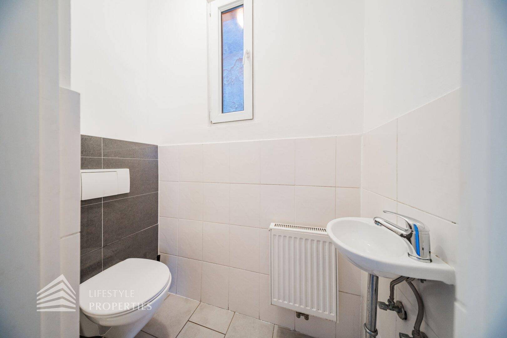 Kleines Gäste-WC mit Toilette, Waschbecken und Fenster für natürliche Belüftung.