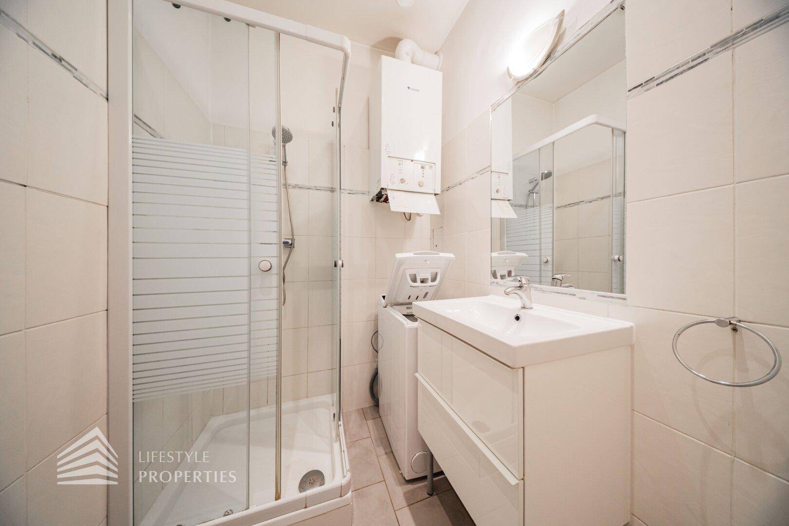 Funktionales Badezimmer mit Duschkabine, Waschbecken und integrierter Waschmaschine.