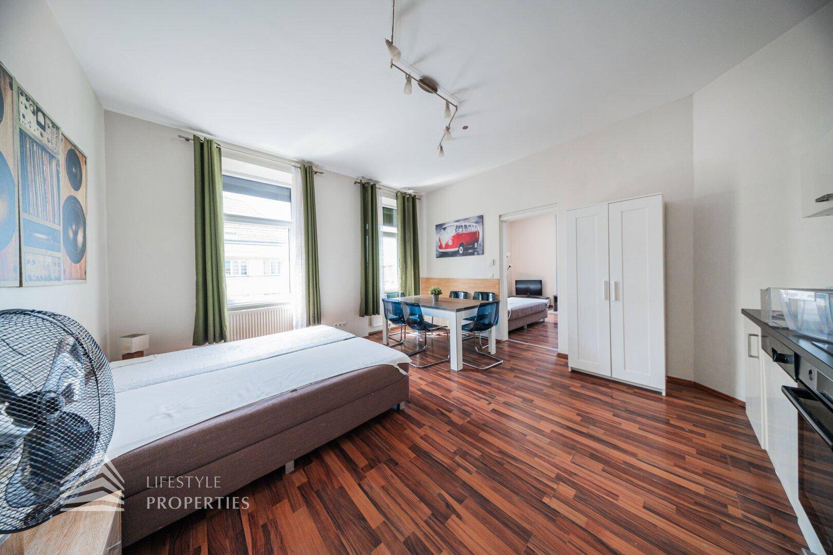 Multifunktionaler Raum mit Betten, Esstisch, Kleiderschrank und integrierter Küchenzeile.