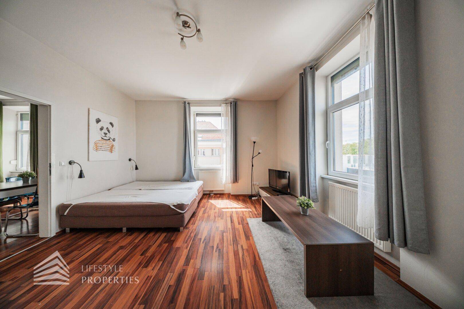 Gemütliches Schlafzimmer mit zwei Einzelbetten, TV-Bereich und großen Fenstern.
