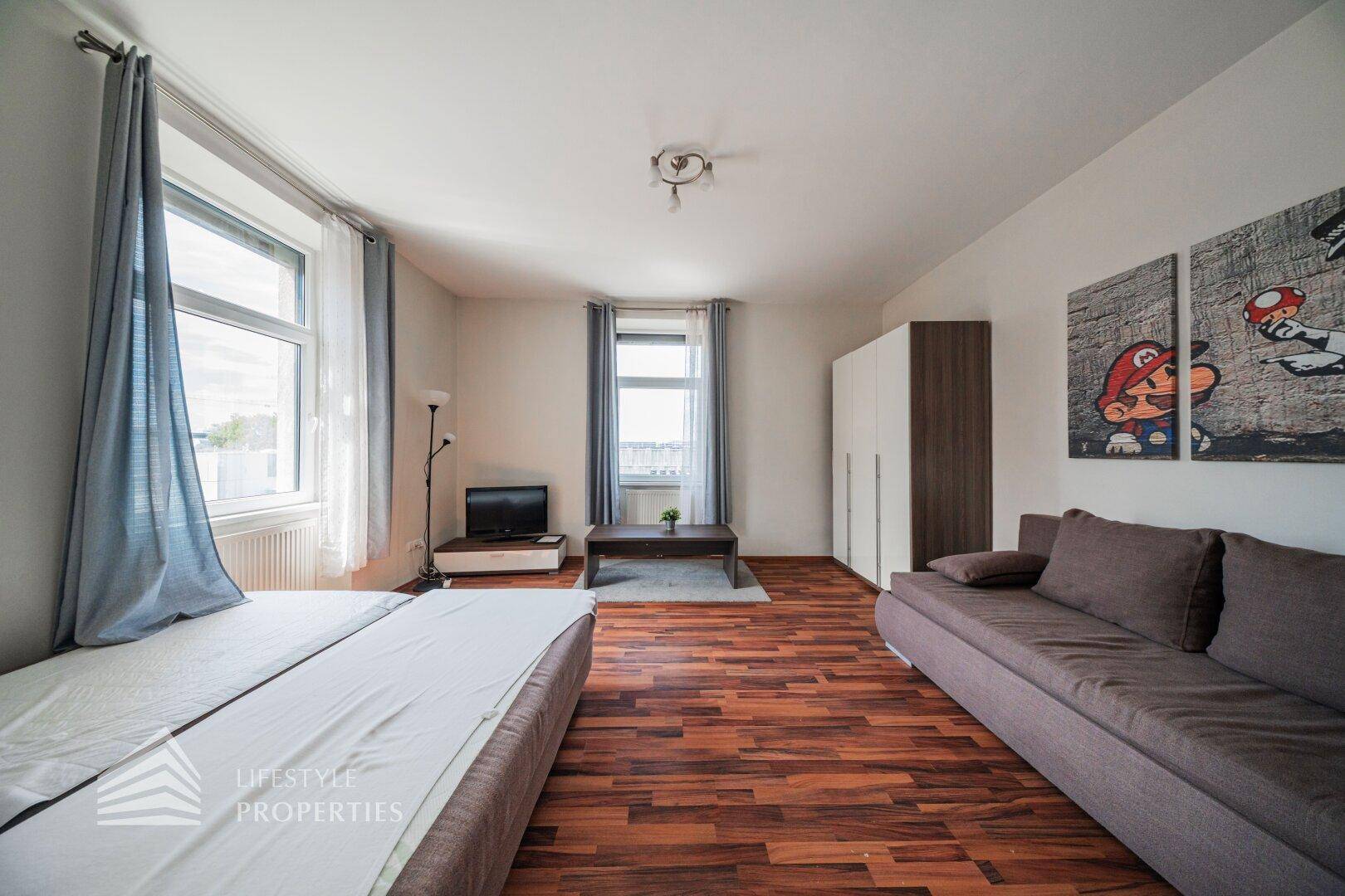 Heller Wohnbereich mit Sofa, Betten, TV und Kleiderschrank, ausgestattet für Komfort.