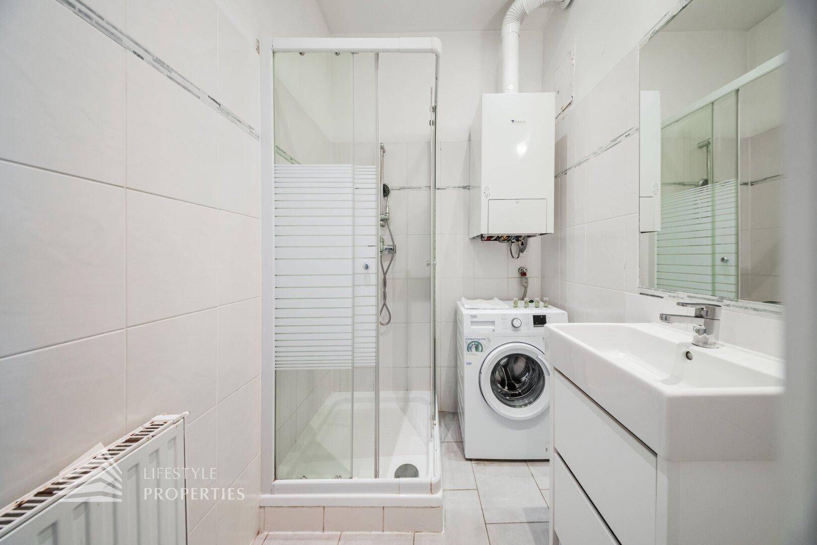 Modernes Badezimmer mit Duschkabine, Waschbecken und Waschmaschine, komplett gefliest.
