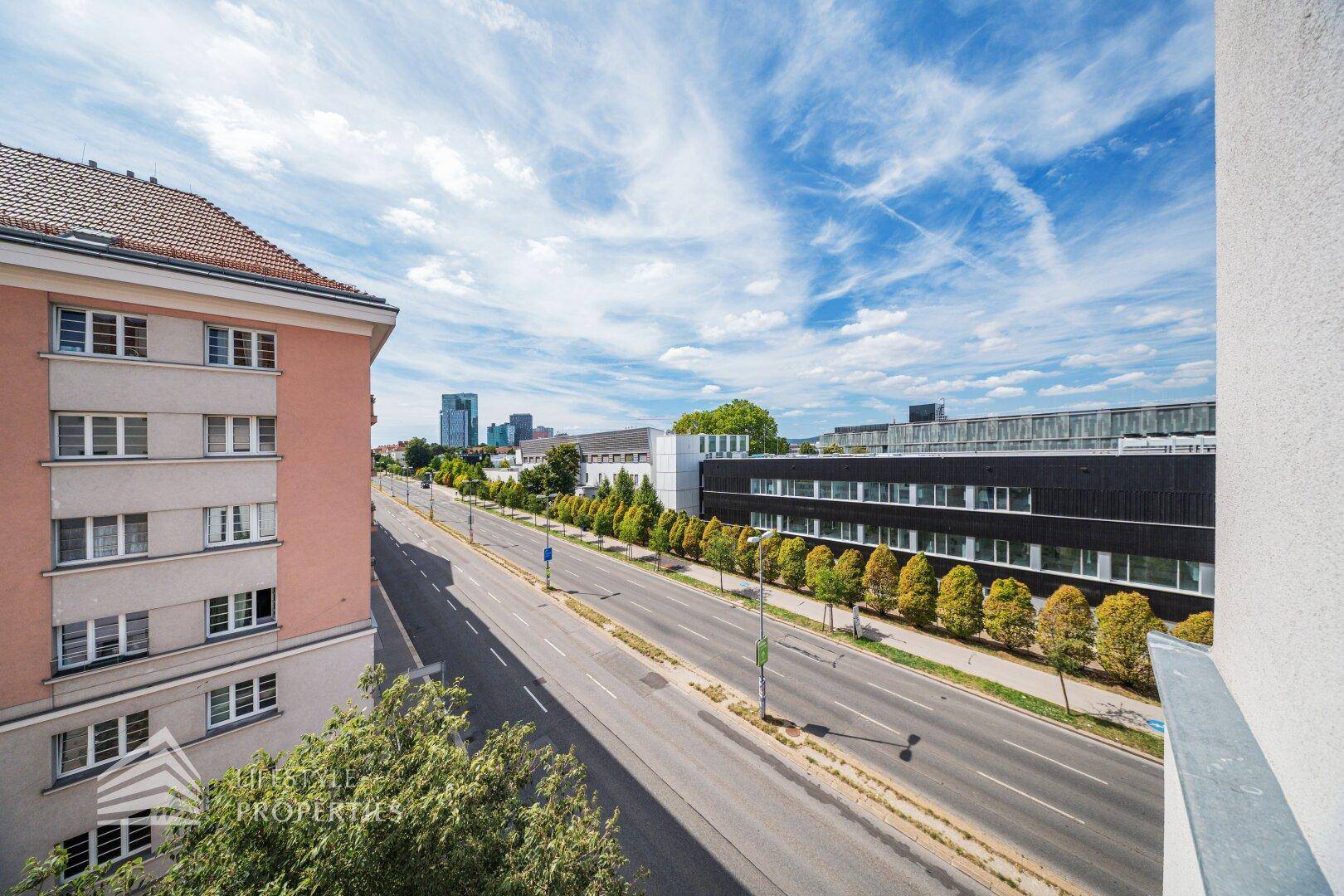 Weitblick über eine Stadtstraße mit Gebäuden und blauem Himmel von einem Balkon aus.