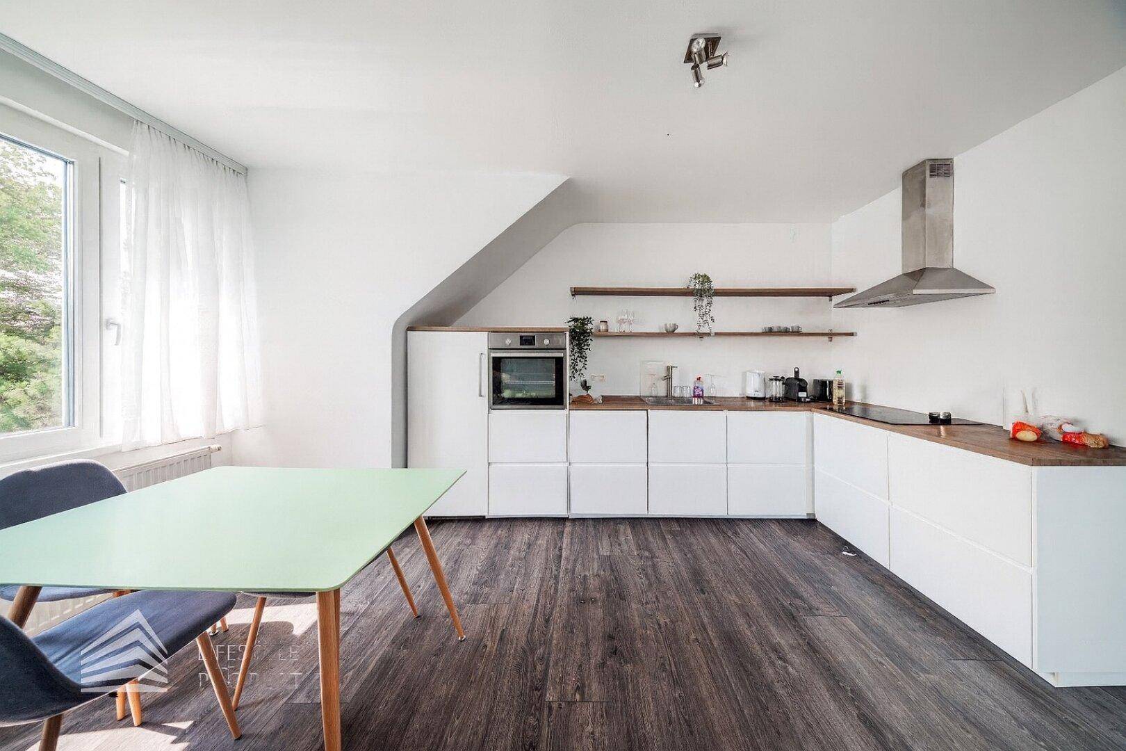 Moderne Küche mit weißen Schränken, Holz-Arbeitsplatten und Essbereich am Fenster.