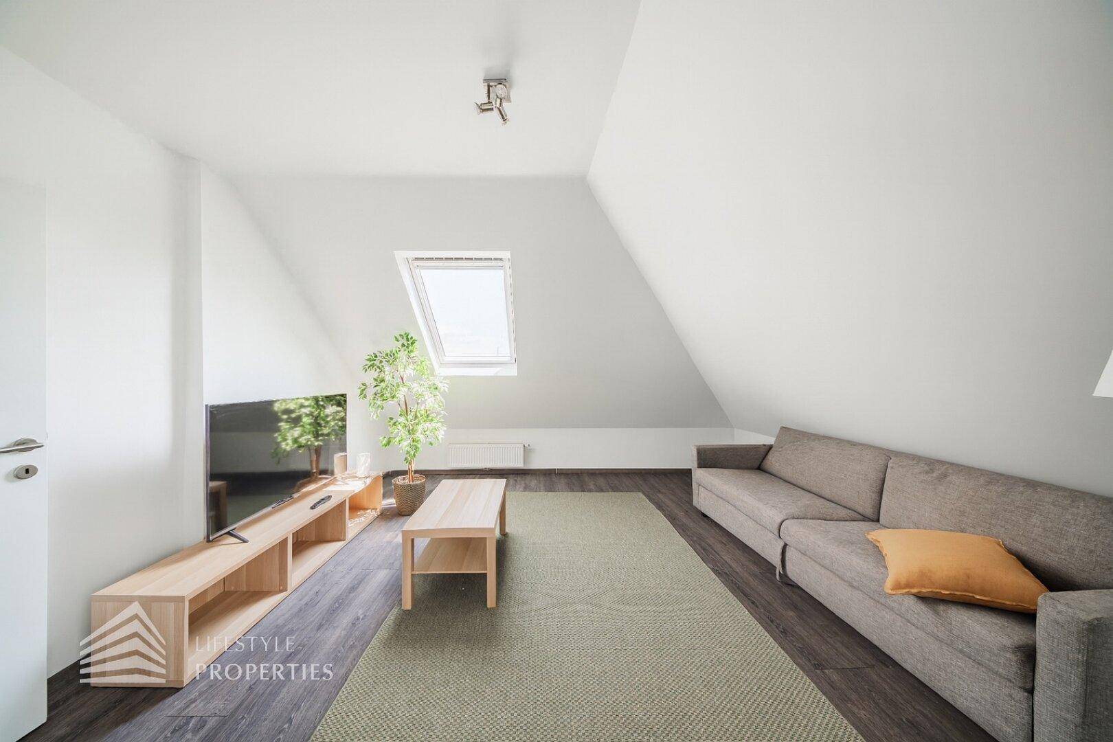 Gemütliches Wohnzimmer im Dachgeschoss mit Sofa, Fernseher und Dachfenster für viel Licht.