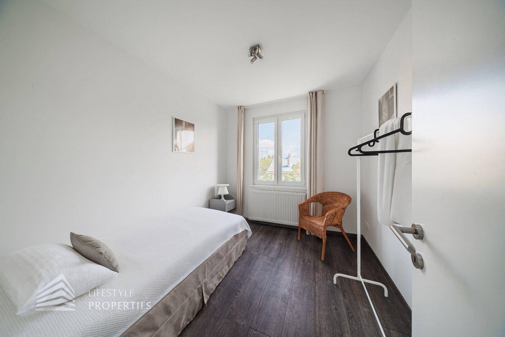 Helles Schlafzimmer mit Einzelbett, Laminatboden und Fenster mit Blick ins Grüne.
