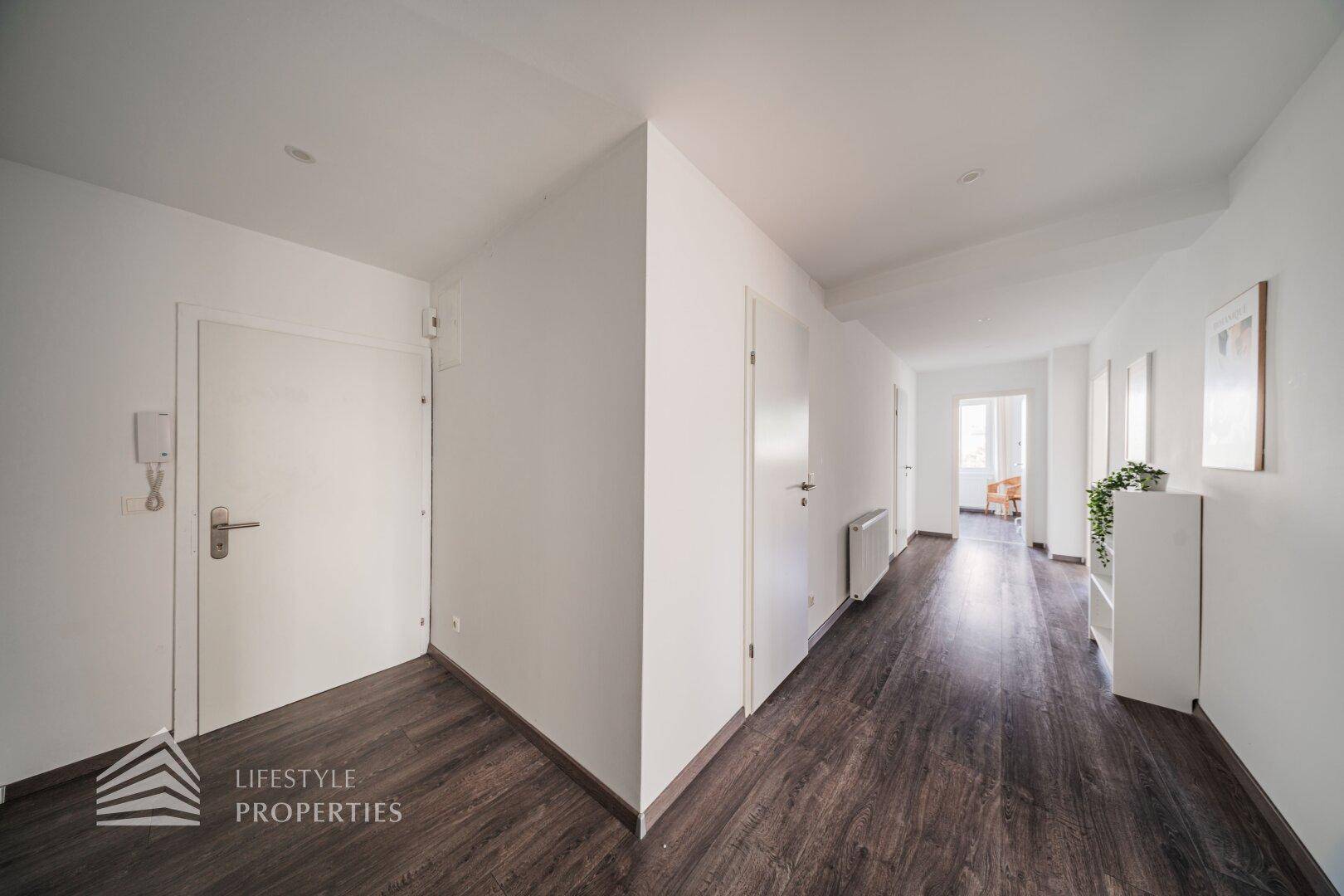 Langer, heller Flur mit dunklem Laminatboden und weiß gestrichenen Wänden.