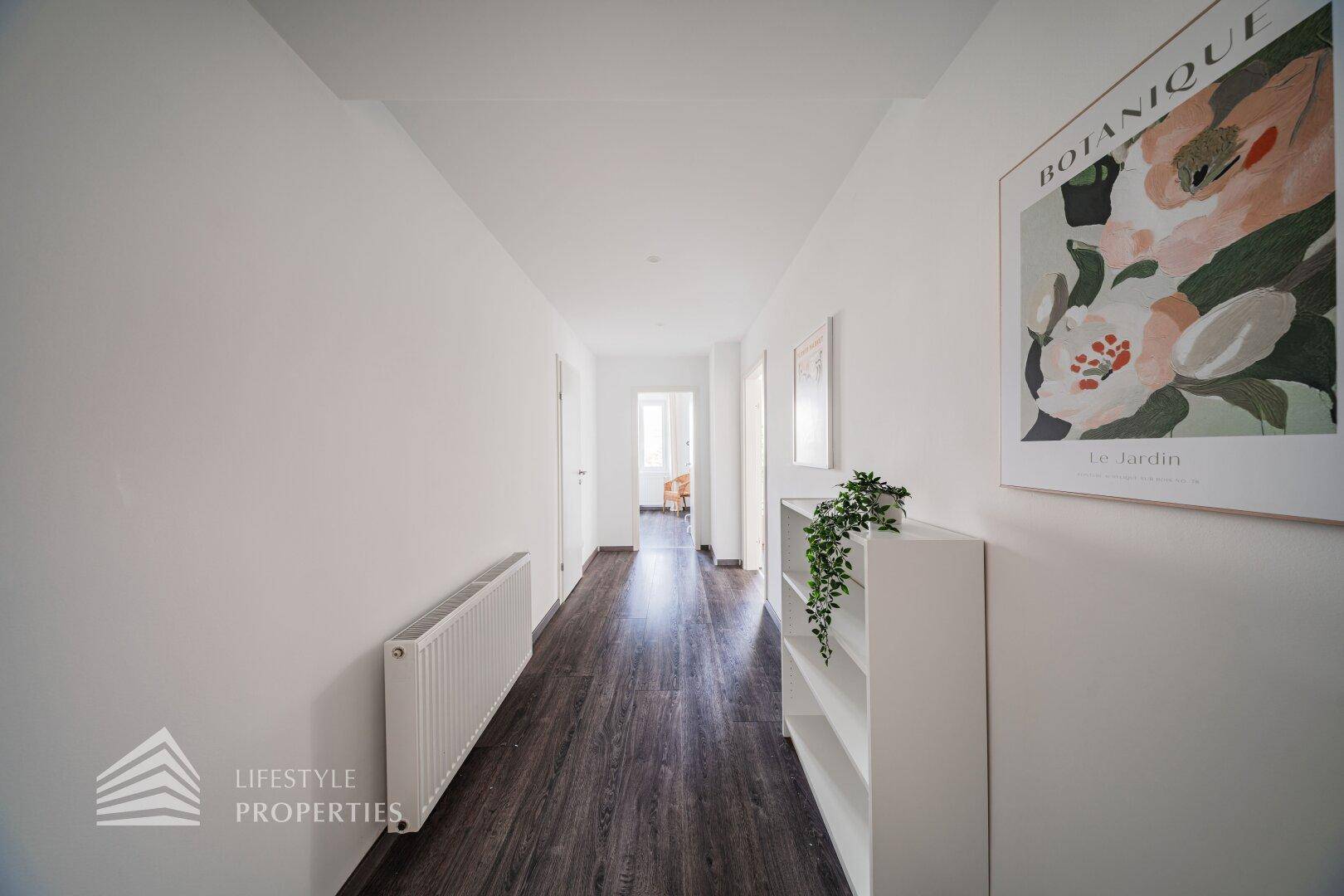 Heller Flur mit dunklem Laminatboden und weiß gestrichenen Wänden, der zu weiteren Räumen führt.
