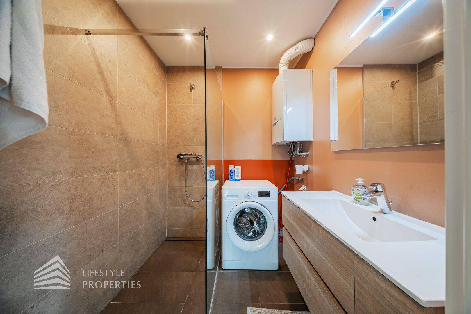 Modernes Badezimmer mit Dusche, Waschmaschine und Waschbecken mit Holzunterschrank.