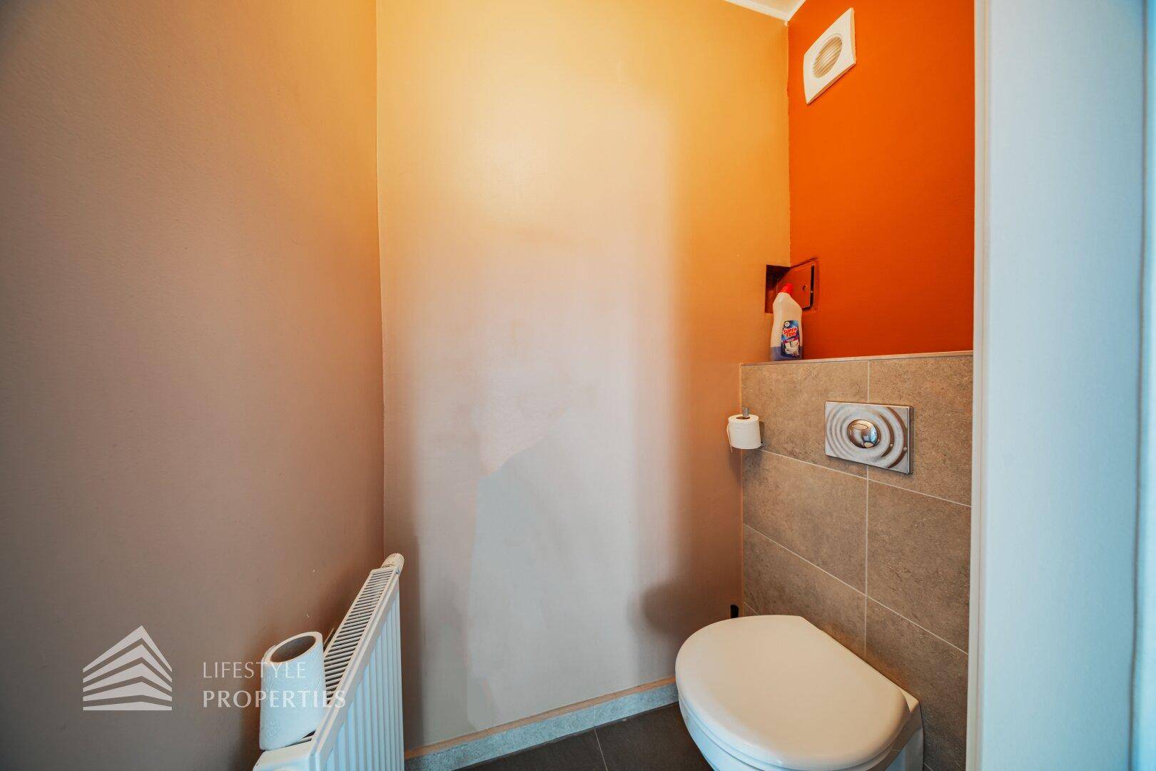 Separate Toilette mit Wand-WC, Heizkörper und farbiger Akzentwand.