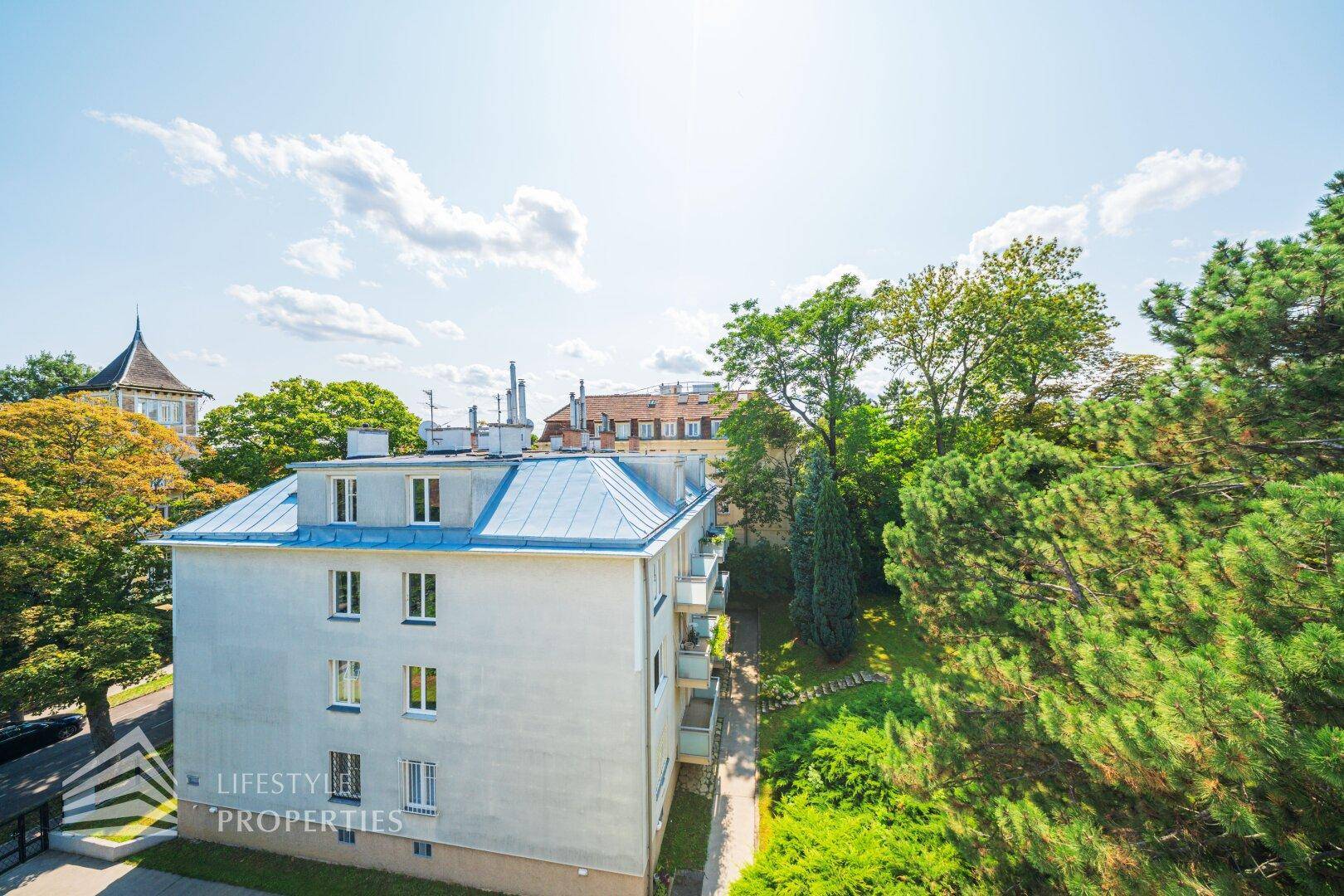 Mehrfamilienhaus mit blauer Dachkonstruktion und grüner Umgebung unter blauem Himmel.