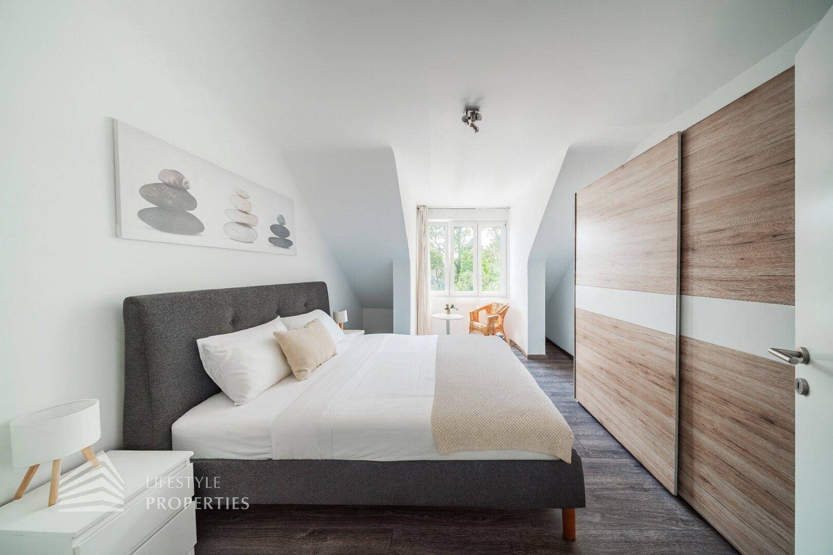 Modernes Schlafzimmer im Dachgeschoss mit großem Bett, Einbauschrank und Fenster.