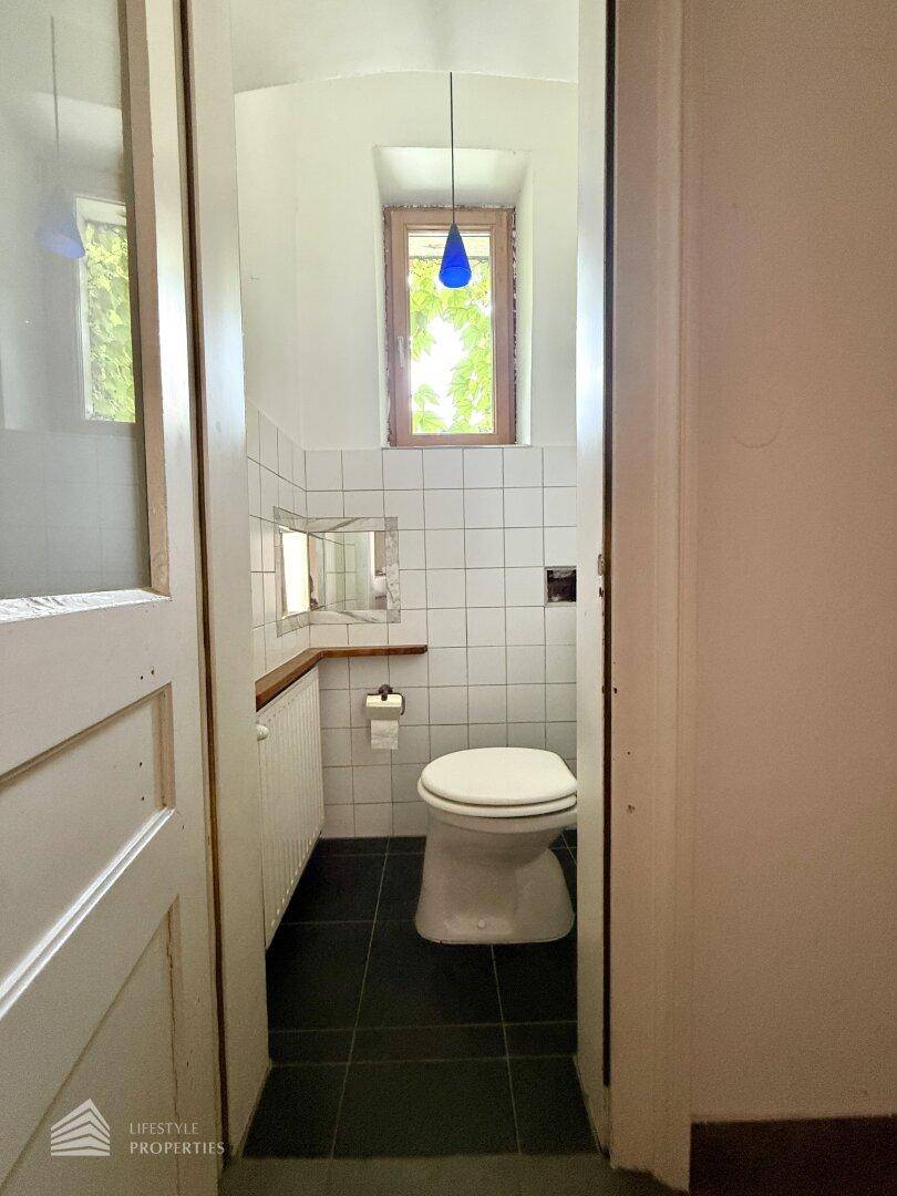 Kleines WC mit Toilette, Heizkörper und Fenster, ausgestattet mit weißen und dunklen Fliesen.