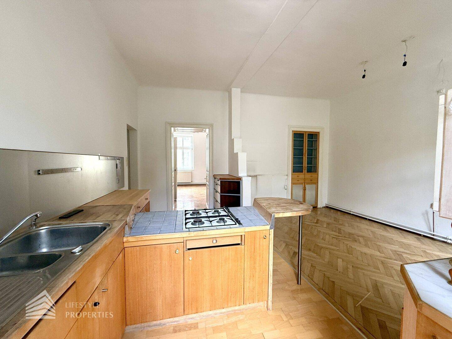 Funktionale Küche mit Holzschränken, Spüle und Gasherd, offen zum angrenzenden Wohnbereich.