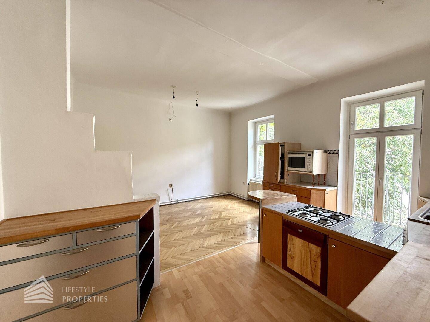 Küche mit Holzmöbeln und Gasherd, angrenzend an einen kleinen Balkon mit Blick ins Grüne.