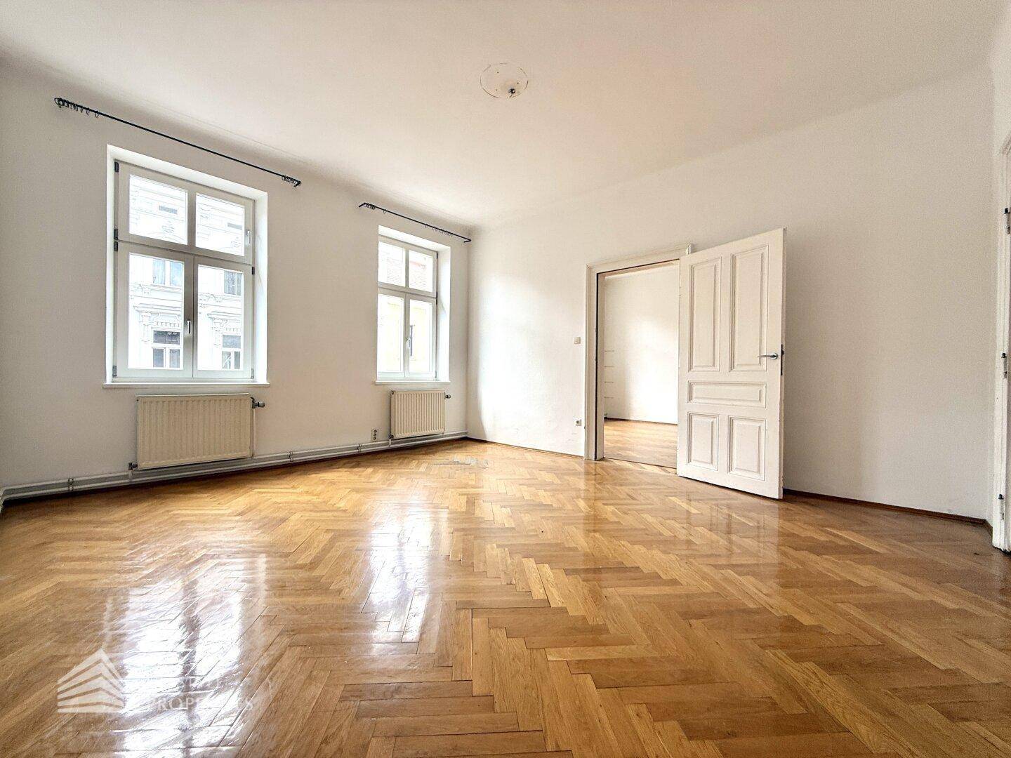 Lichtdurchflutetes Zimmer mit klassischem Fischgrätparkett und hohen Decken, bietet vielseitige Nutzungsmöglichkeiten.
