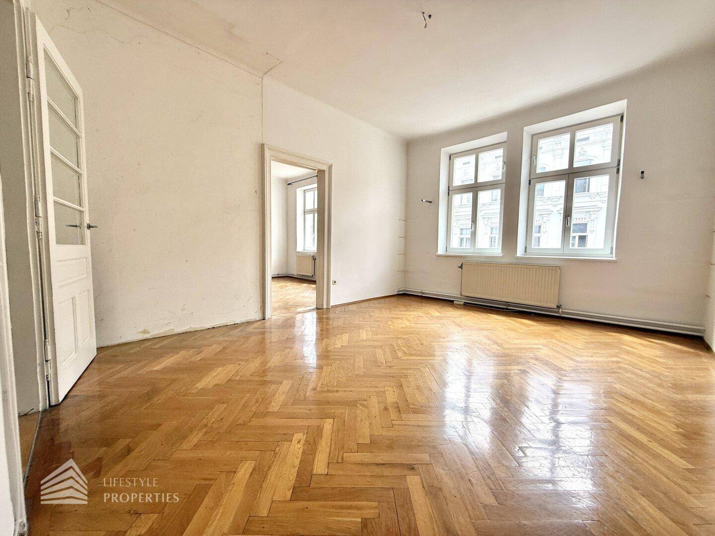 Geräumiges Zimmer mit glänzendem Fischgrätparkett und hohen Fenstern, ideal für Wohn- oder Schlafbereich.