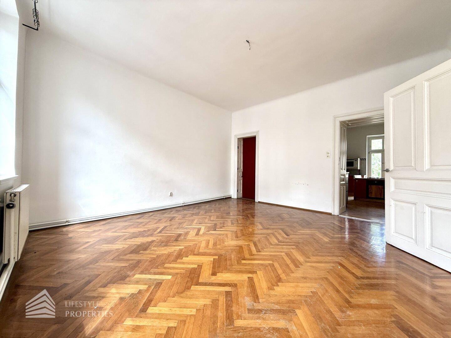 Großzügiges Zimmer mit Fischgrätparkett und hohen Decken, ideal für einen geräumigen Wohnbereich.