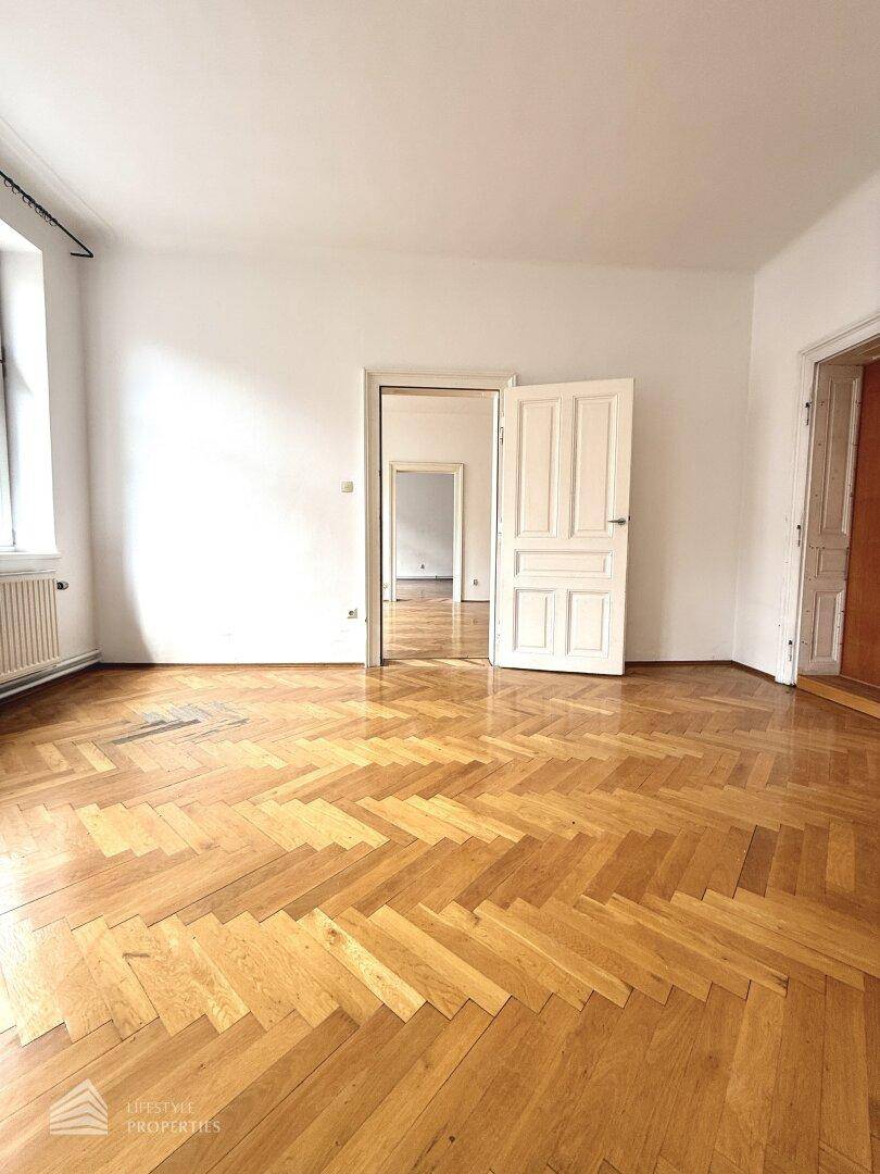 Weitläufiges Zimmer mit klassischem Fischgrätparkett und weiß gestrichenen Wänden, bereit zur Einrichtung.