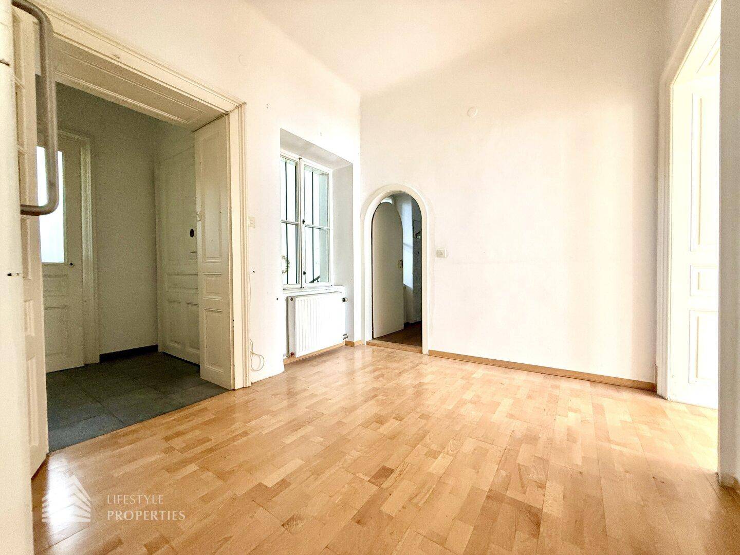 Helles Zimmer mit Holzdielenboden und Rundbogen, verbindet verschiedene Bereiche der Wohnung.