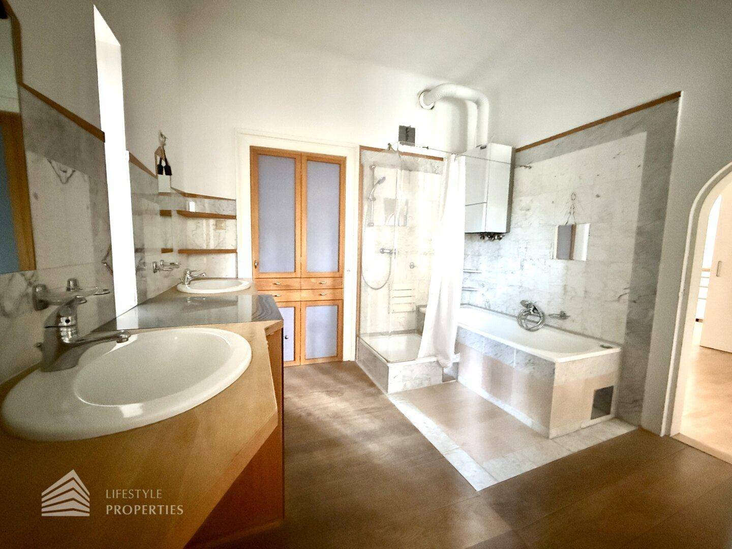 Geräumiges Badezimmer mit zwei Waschbecken, Dusche und Badewanne, verziert mit Marmorfliesen.