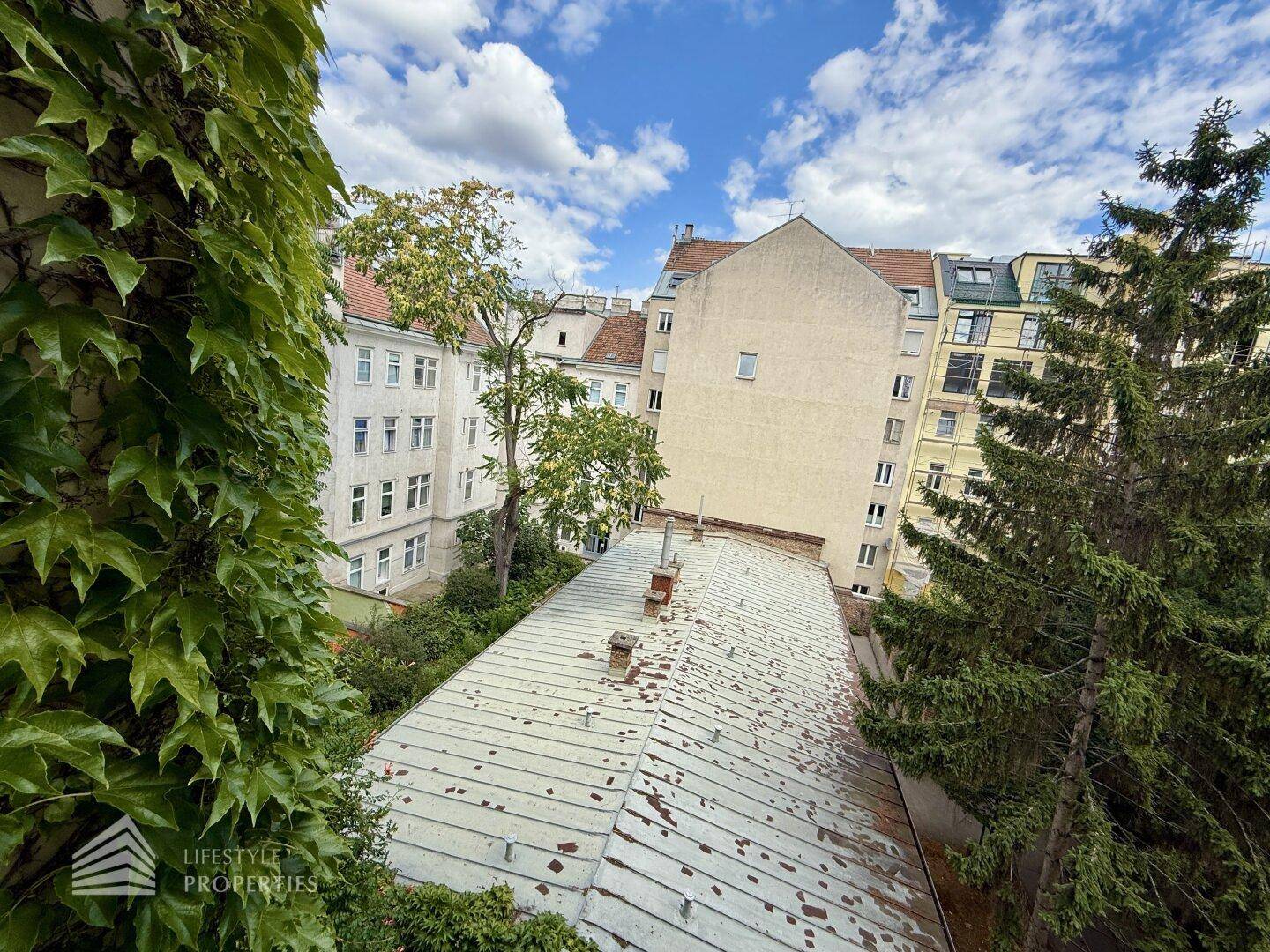 Blick über Dächer und Bäume auf umliegende Gebäude unter einem blauen Himmel.