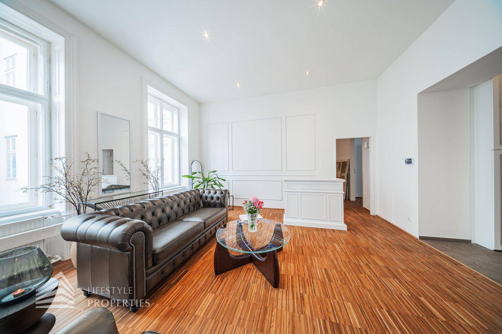 Elegantes Wohnzimmer mit braunem Ledersofa, Holzboden und hohen Fenstern, die den Raum mit Licht durchfluten.