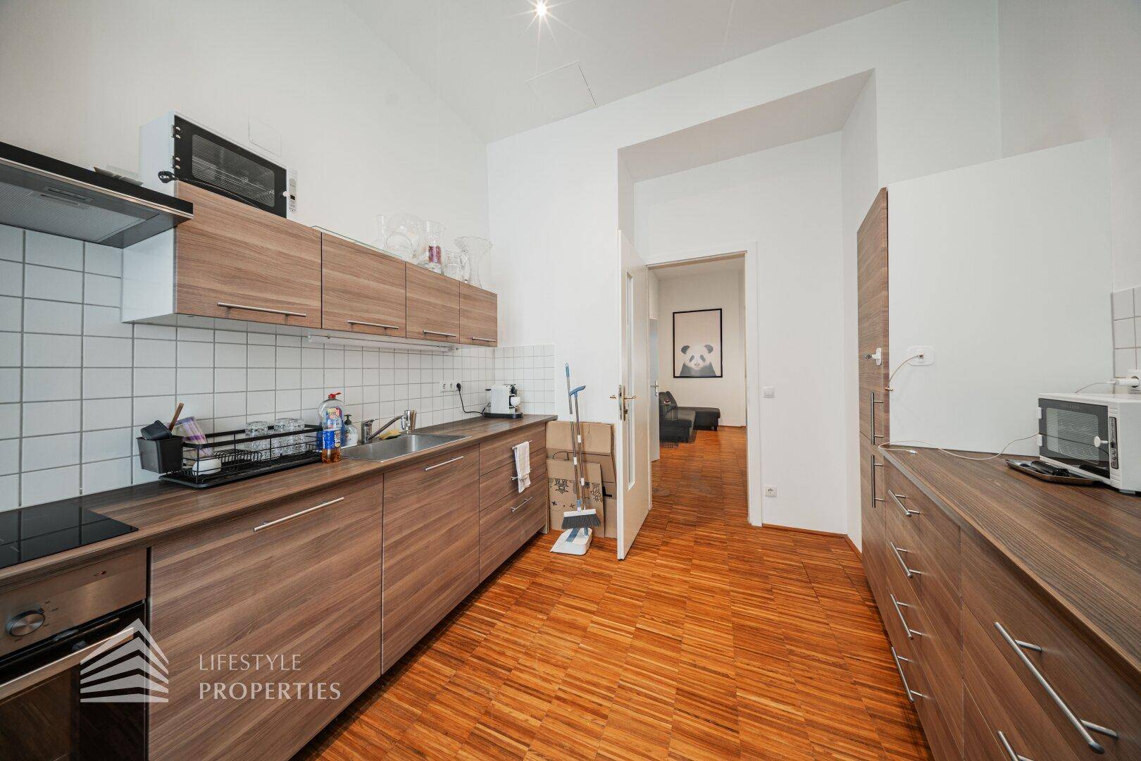 Praktische Küche mit Holzfronten, Edelstahlspüle und Blick in einen angrenzenden Raum, ideal für den täglichen Gebrauch.