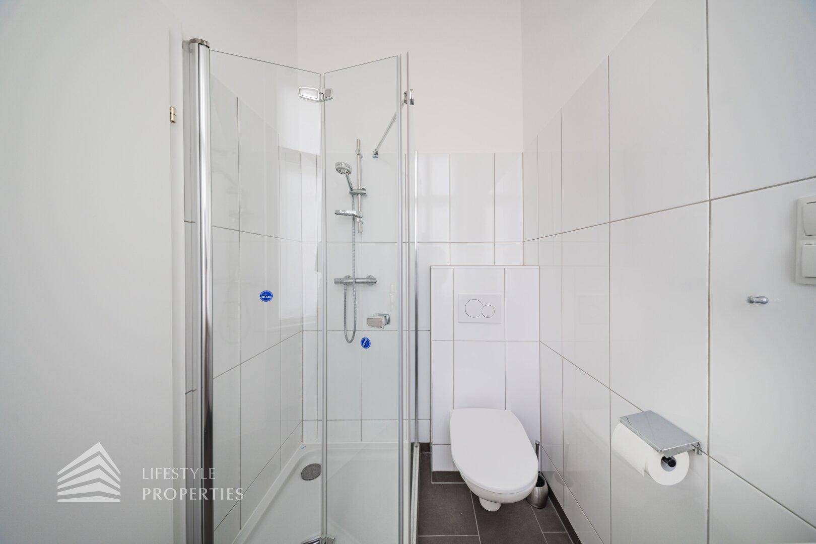 Modernes Badezimmer mit Duschkabine, wandhängender Toilette und weißen Fliesen, das eine saubere Ästhetik bietet.