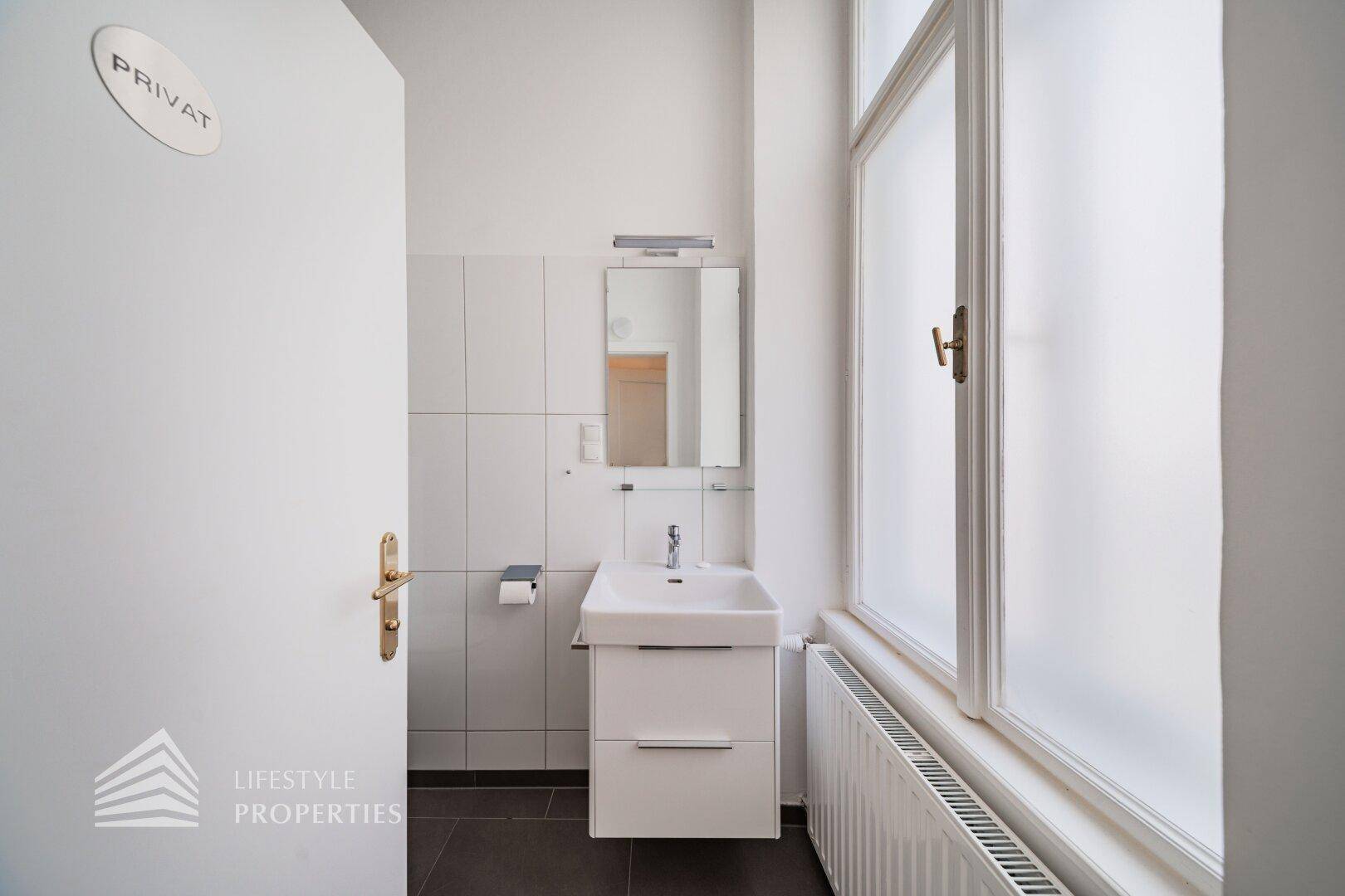 Helles Badezimmer mit Waschbecken, Spiegel und einem großen Milchglasfenster, das Privatsphäre und Licht bietet.
