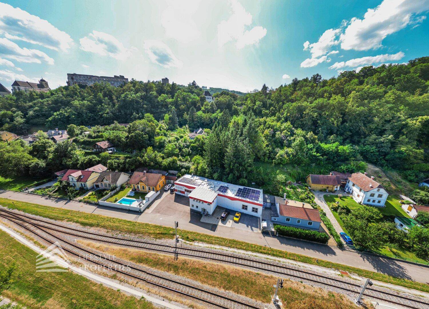 Panoramablick aus der Luft auf das Gewerbegebäude, umgeben von Natur, Bahnlinien und Wohngebäuden.