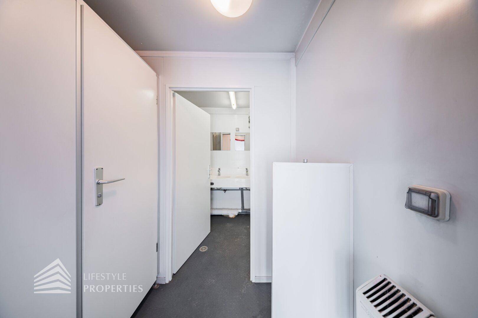 Schmaler Flur mit weiß gestrichenen Wänden, der zu einem Badezimmer oder Waschraum führt.