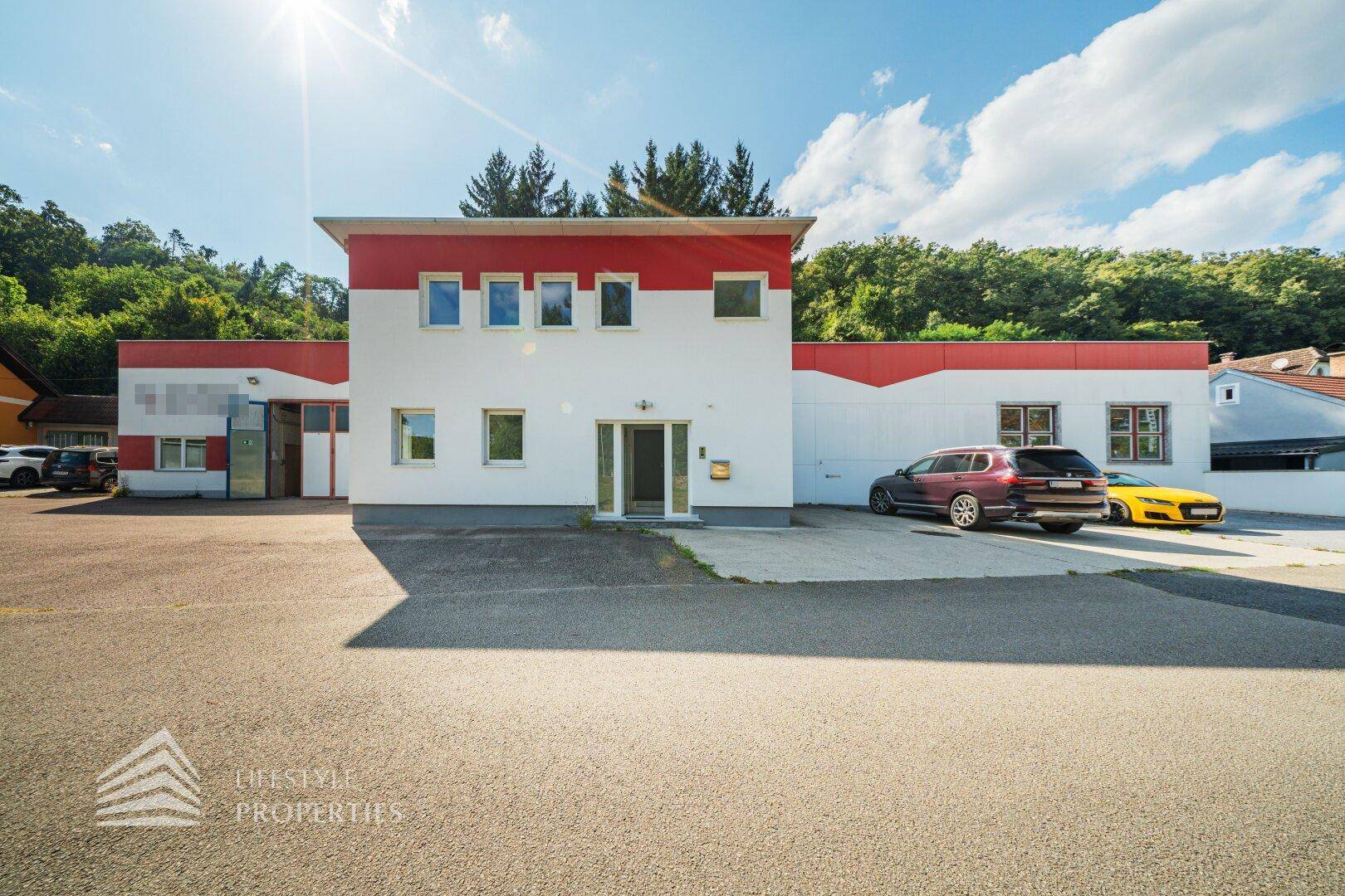 Vorderansicht des Gewerbegebäudes mit roter Akzentfassade und Parkplätzen unter strahlendem Sonnenschein.