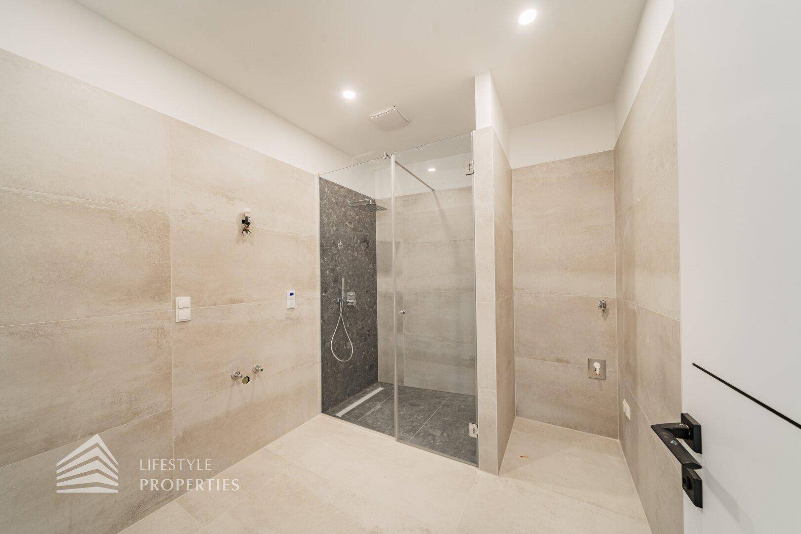 Modernes Badezimmer mit beigefarbenen Fliesen und einer geräumigen begehbaren Dusche mit Glaswand.