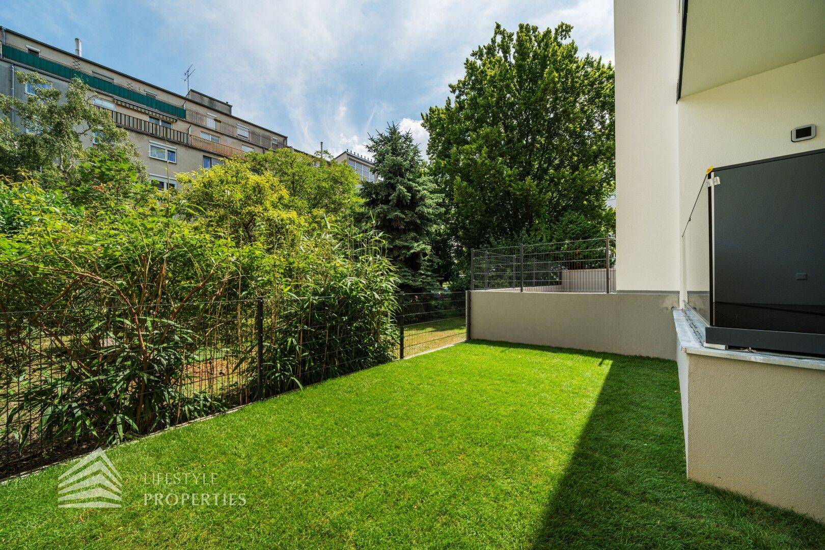 Kleiner privater Gartenbereich mit Rasenfläche und umzäunter Bepflanzung hinter dem Gebäude.