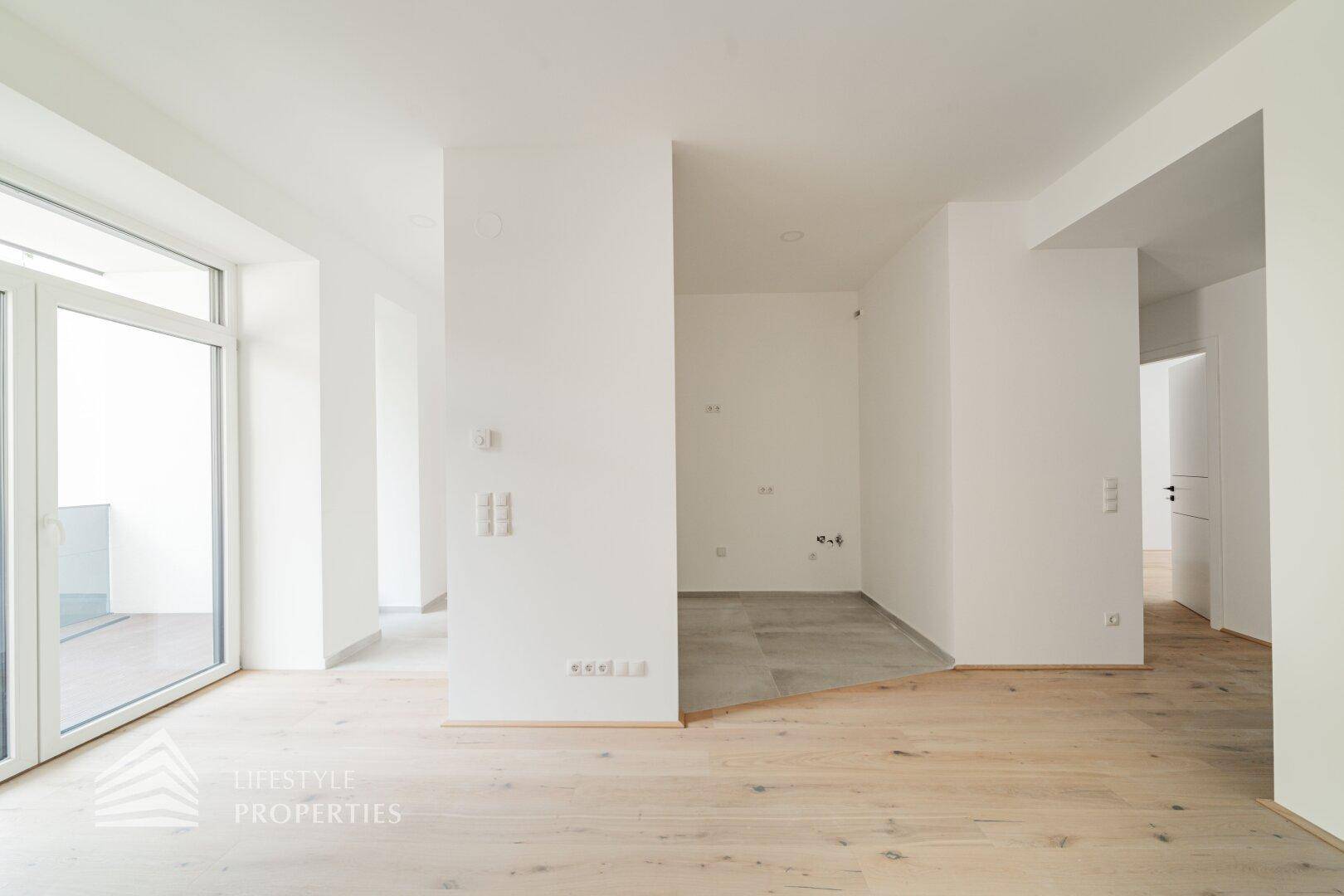 Heller Wohnbereich mit Holzboden, der in einen gefliesten Bereich übergeht, mit viel Tageslicht.