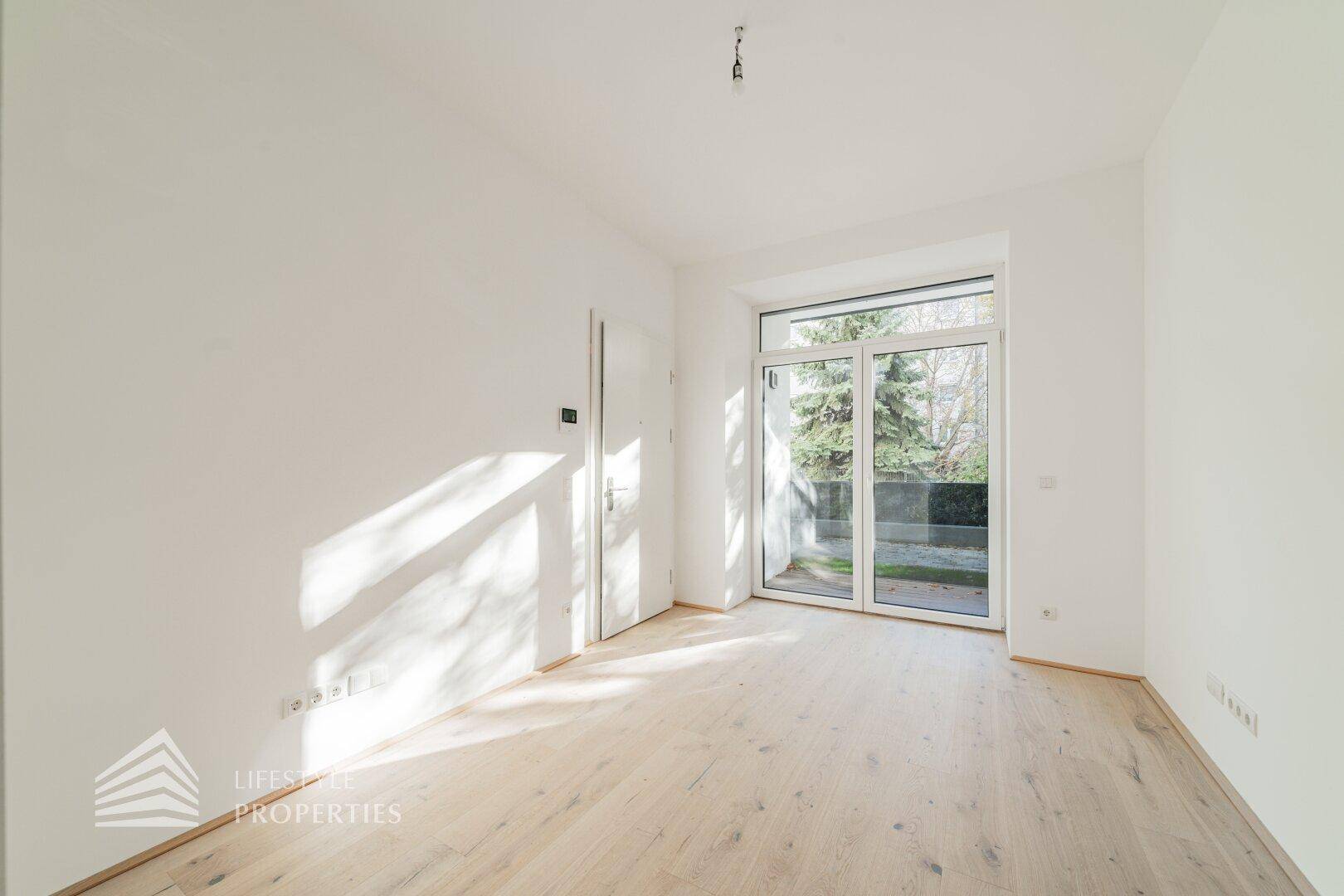Heller Raum mit Holzboden und einer großen Glastür, die Zugang zu einem Außenbereich bietet.