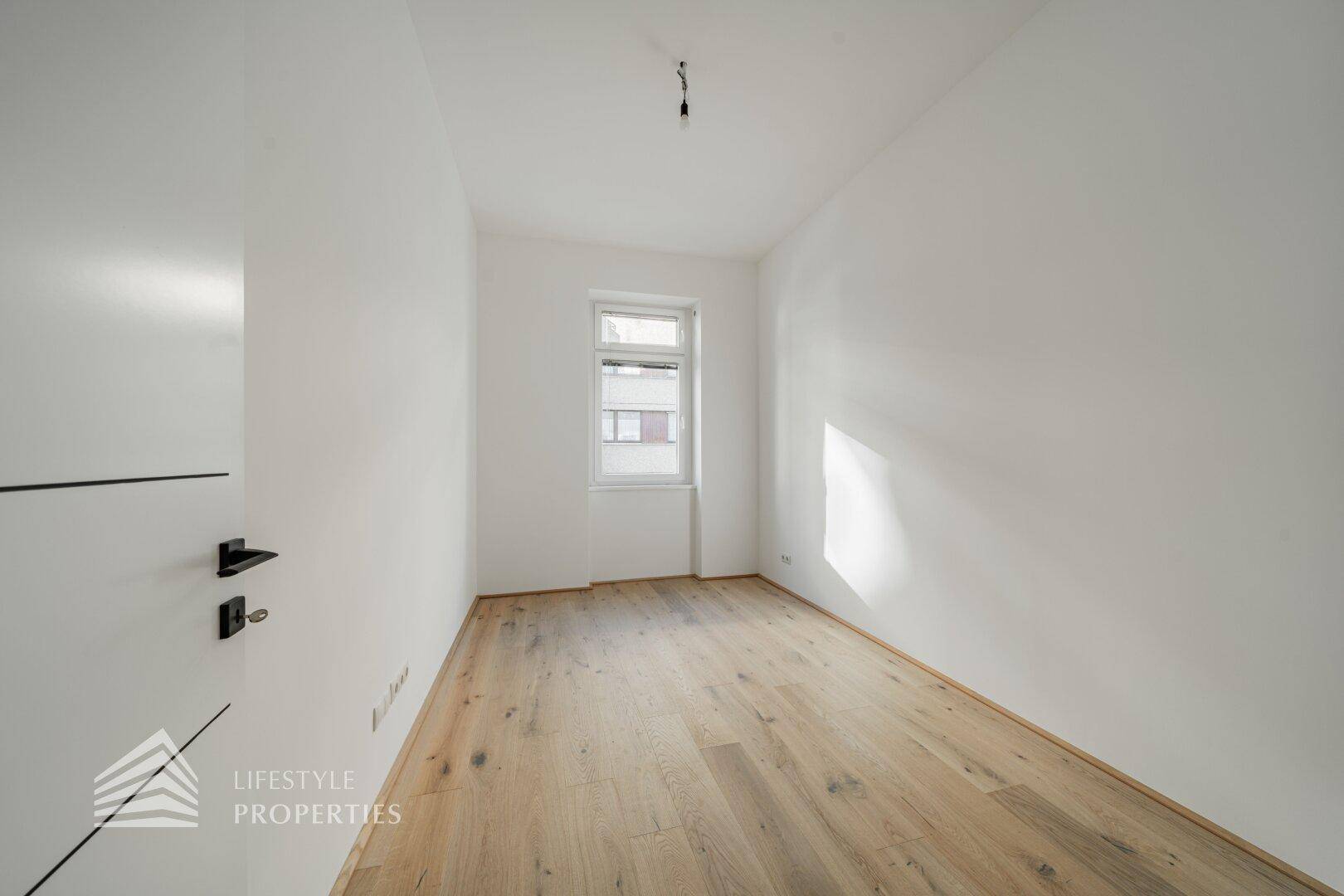 Kleinerer, heller Raum mit Holzboden und einem Fenster, ideal als Schlaf- oder Arbeitszimmer.