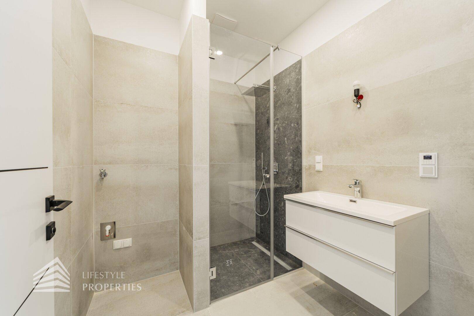 Helles Badezimmer mit moderner Waschtischkonsole, begehbarer Dusche und beigefarbenen Wandfliesen.