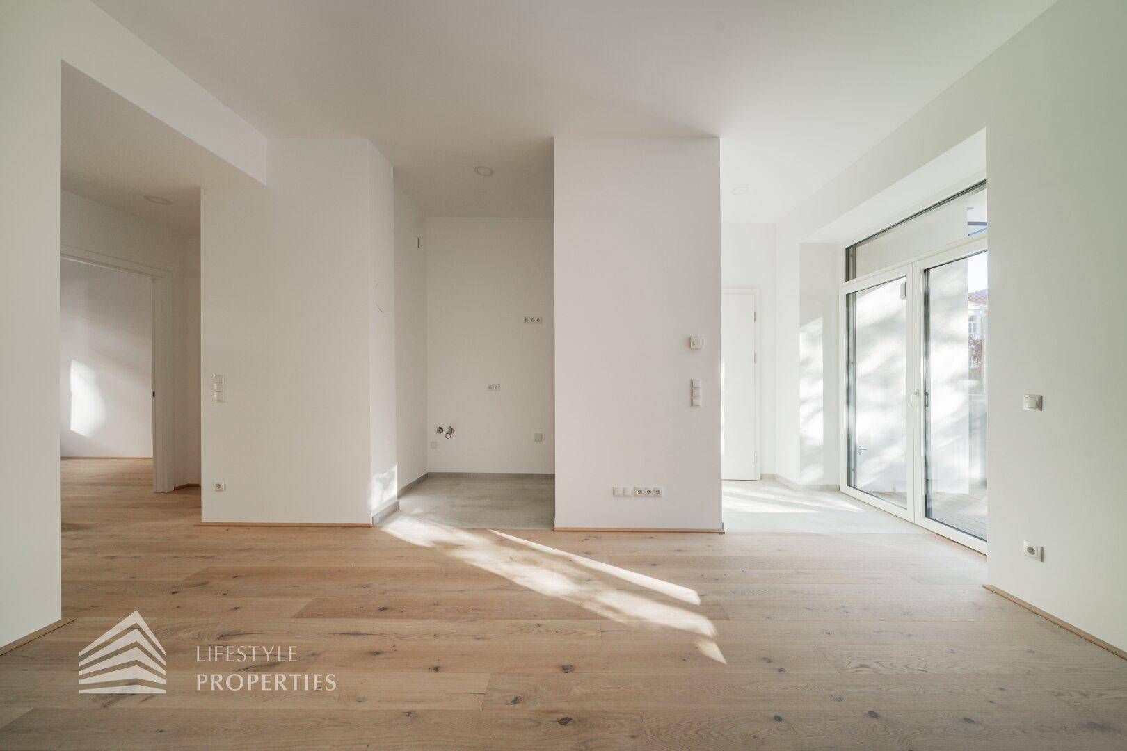 Offener Wohnbereich mit Holzboden, der in einen gefliesten Bereich übergeht, mit viel Tageslicht.