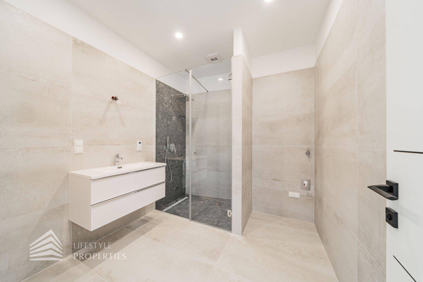 Modernes Badezimmer mit Waschtisch und begehbarer Dusche, ausgestattet mit hellen Fliesen.