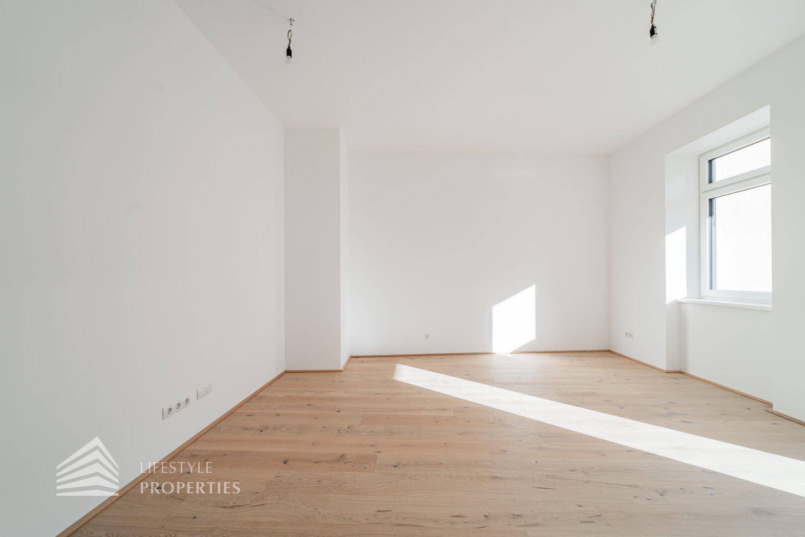 Heller, leerer Raum mit Holzboden und einem Fenster, das den Raum mit Sonnenlicht durchflutet.