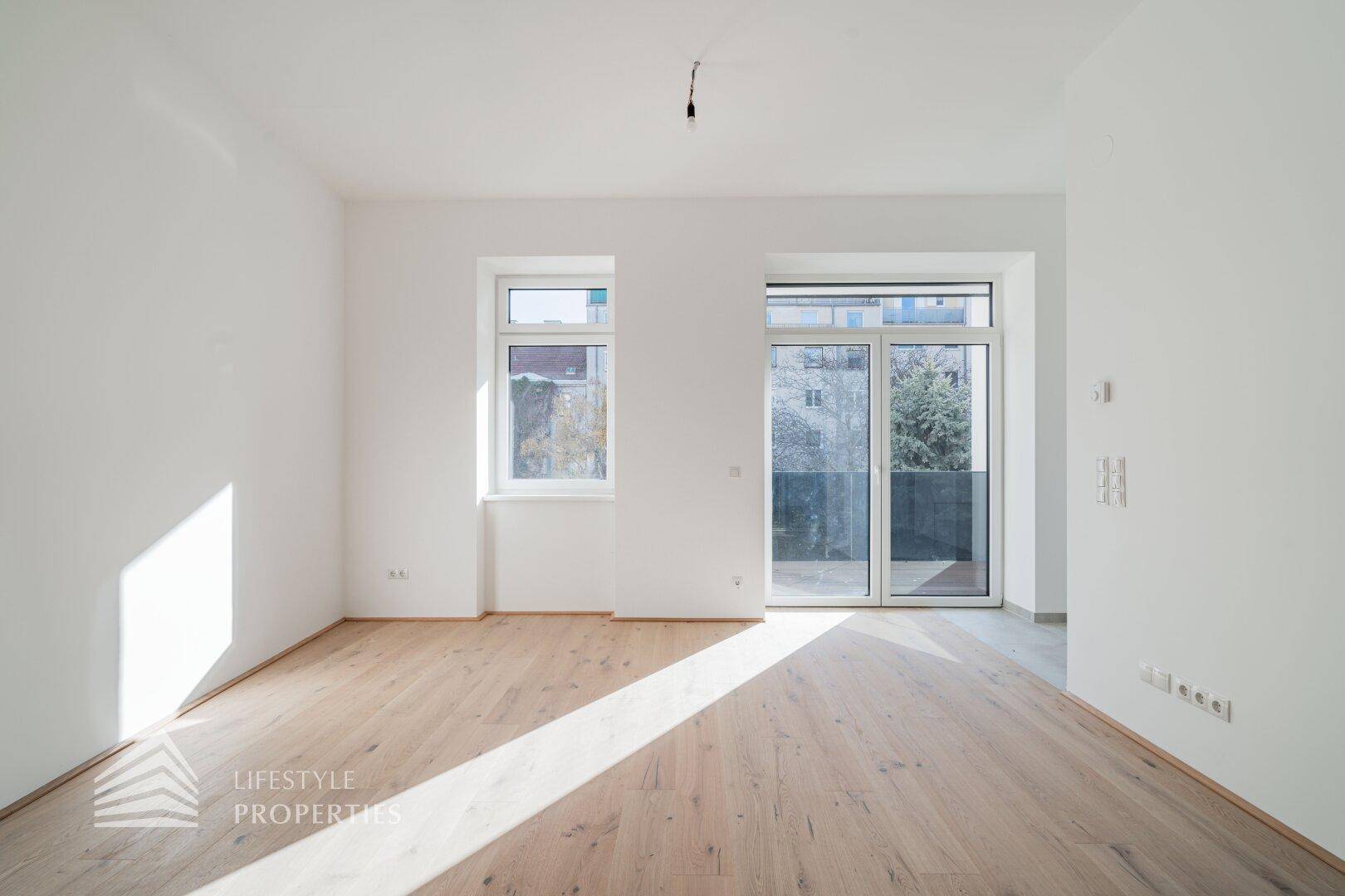 Heller Raum mit Holzboden, einem Fenster und einer Glastür, die Zugang zu einem Außenbereich bietet.