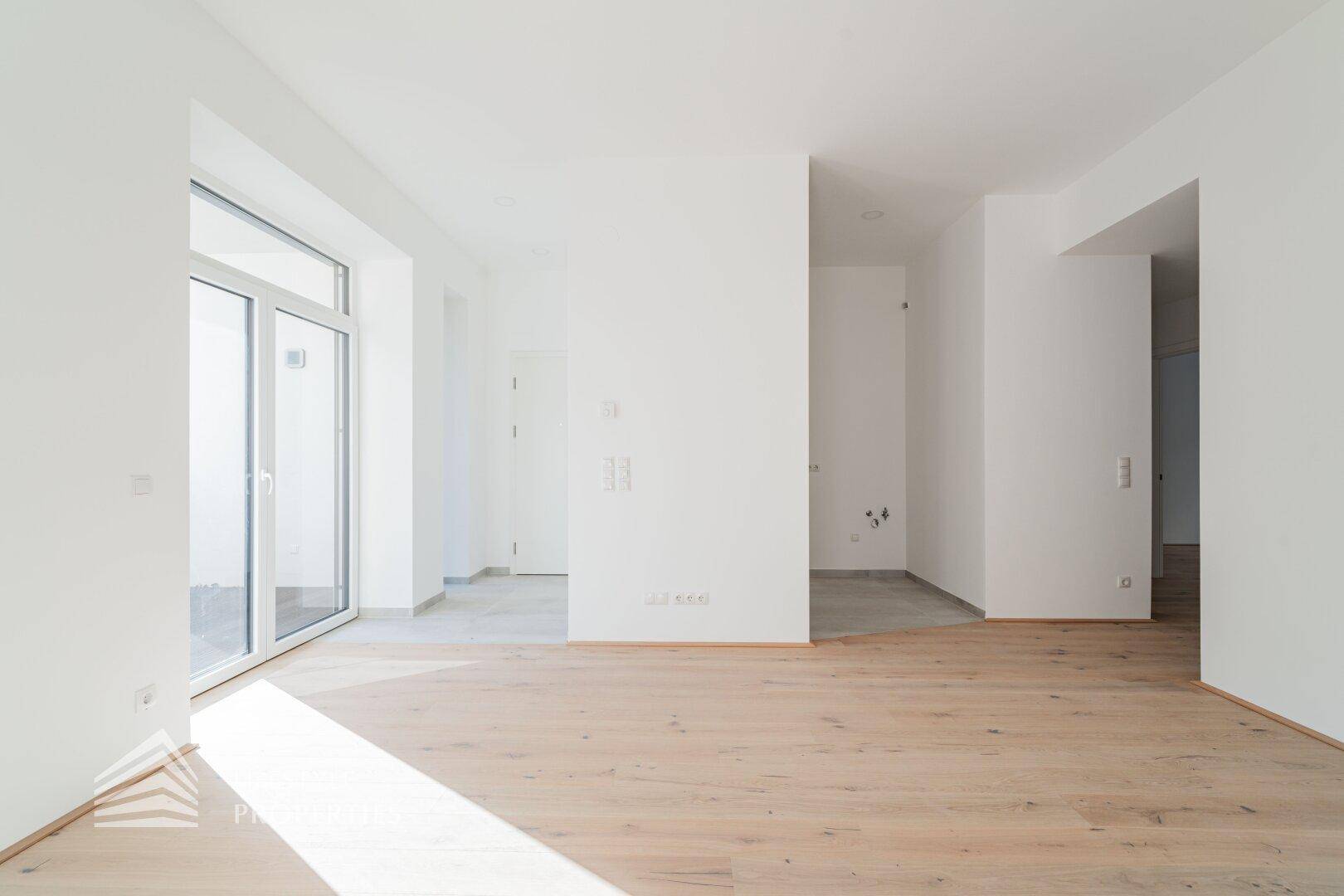Offener Wohnbereich mit Holzboden, der in einen gefliesten Bereich übergeht, mit viel Tageslicht.