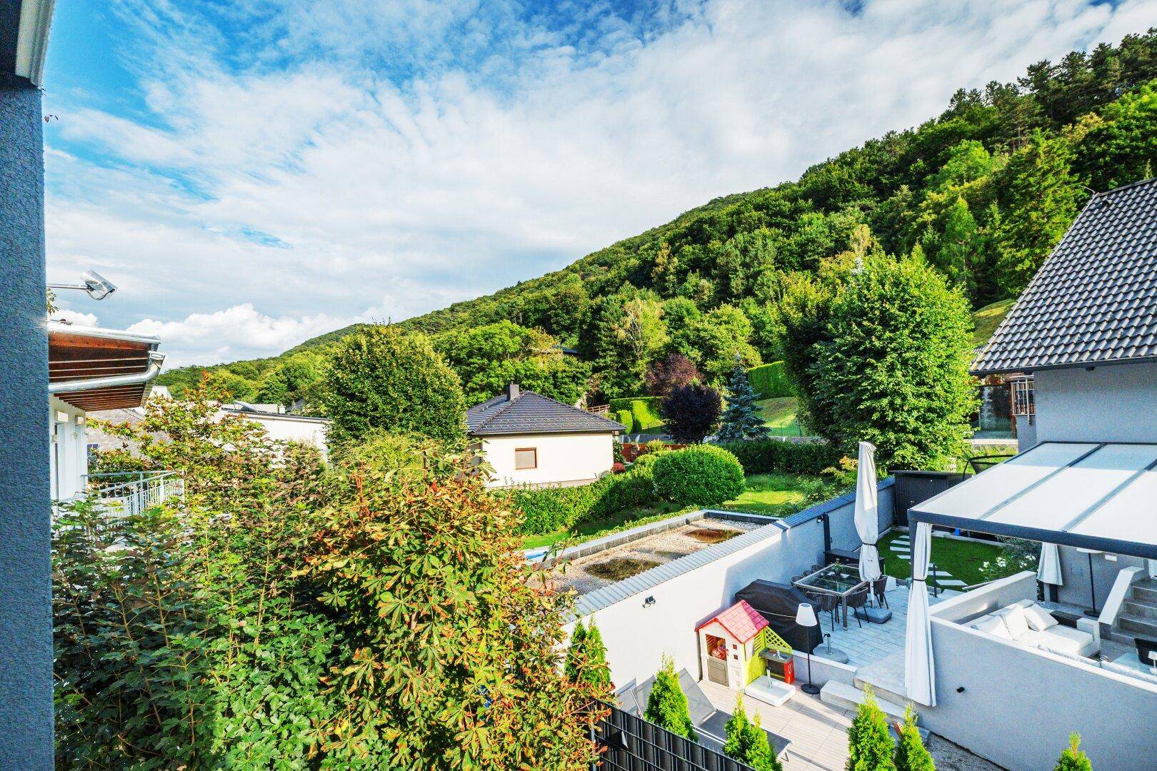 Panoramablick von einer Terrasse auf eine grüne Hügellandschaft und benachbarte Gärten.