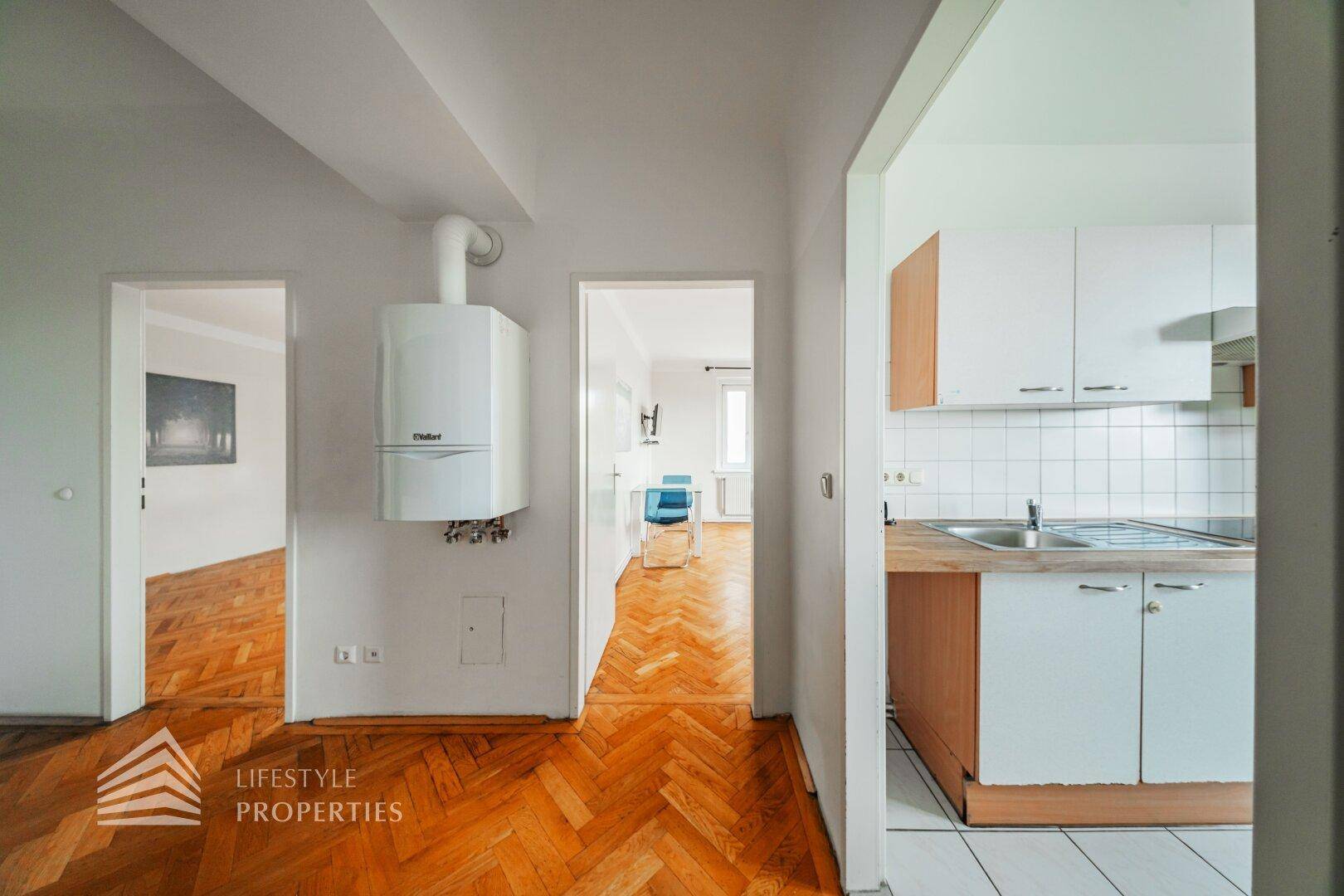 Flur mit Fischgrätparkett, Heiztherme und Blick in die angrenzende Küche und ein weiteres Zimmer.