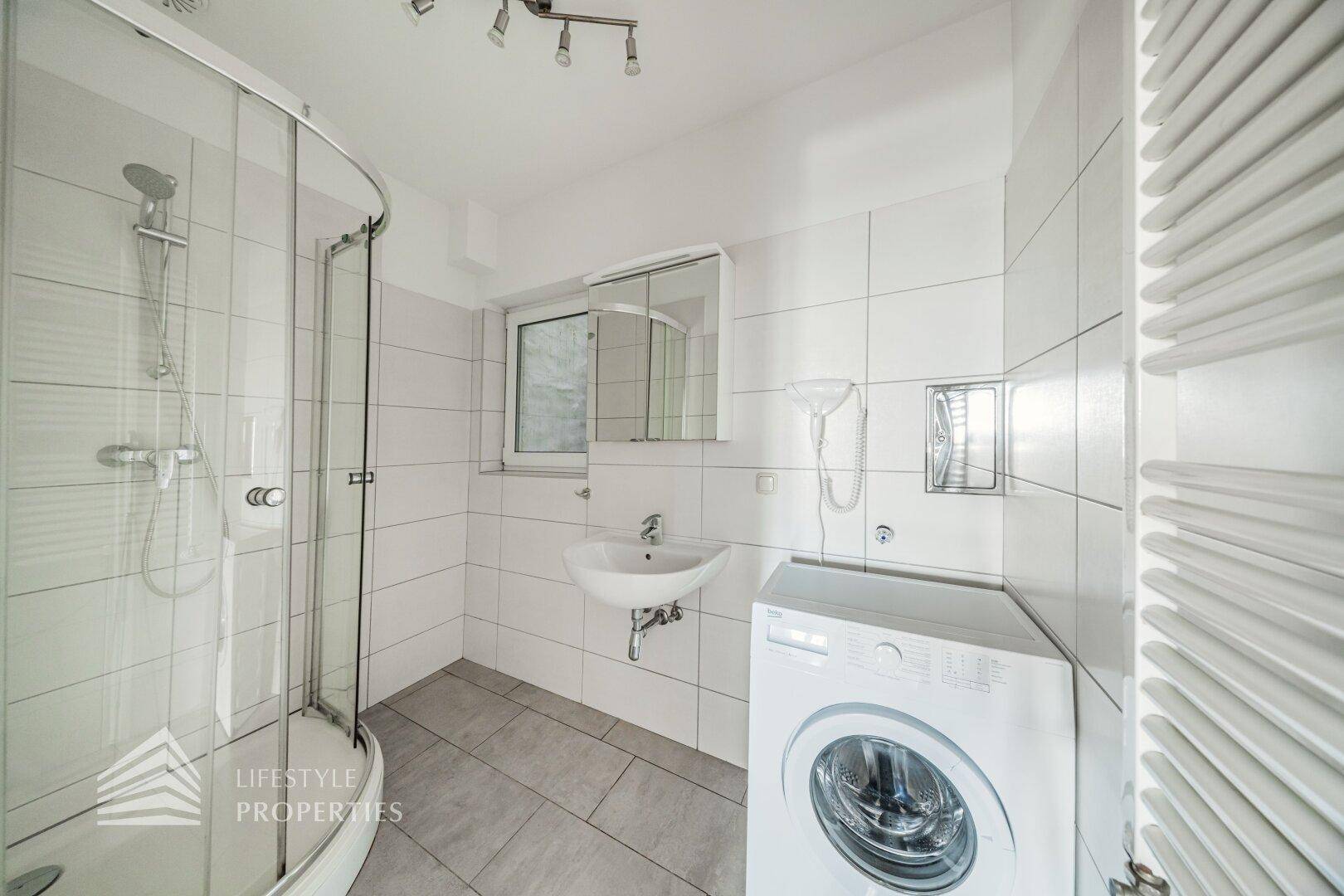 Modernes Badezimmer mit Dusche, Waschbecken, Waschmaschine und beheiztem Handtuchhalter für Komfort.