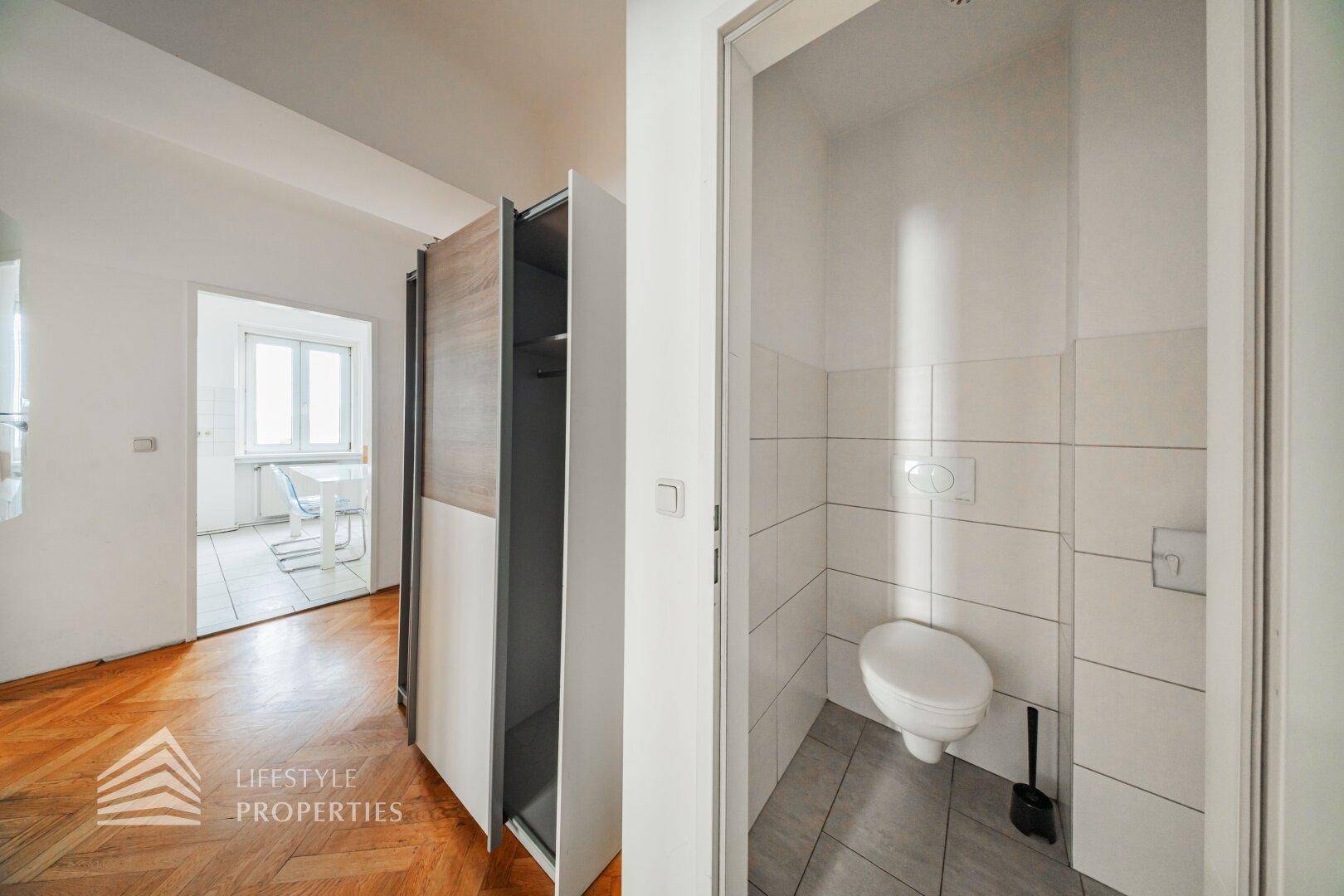 Separate Gästetoilette mit Wand-WC, Spülkasten und hellen, modernen Fliesen an Wänden und Boden.