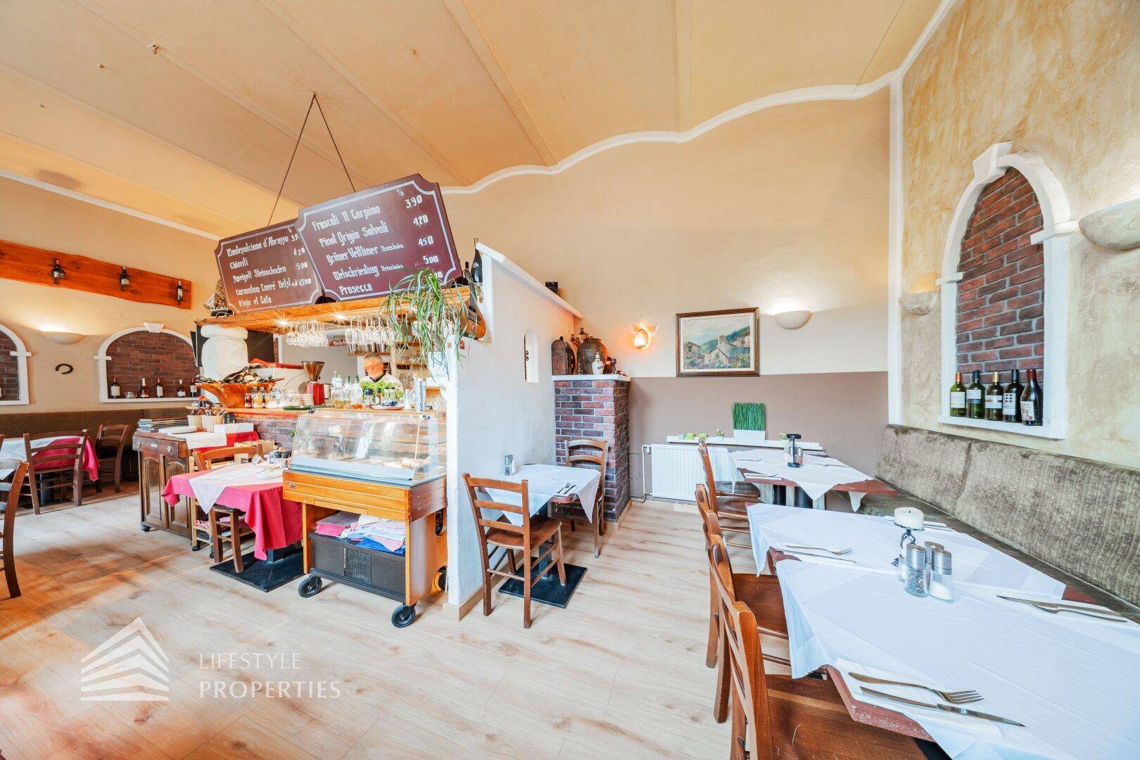 Blick auf den Thekenbereich und die Speisesäle eines Restaurants mit Holzboden und traditioneller Einrichtung.