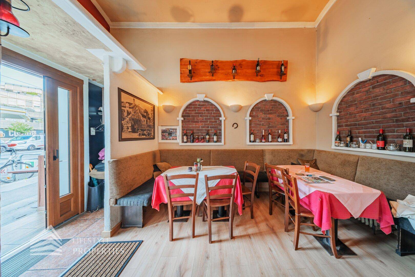 Eingangsbereich und gemütliche Sitzecke eines Restaurants mit Ziegelnischen und Holzboden.